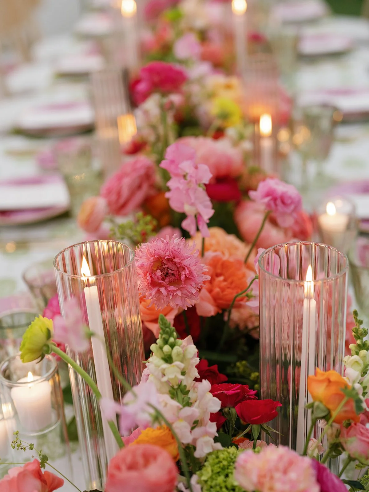  Close-up table setting with pink and coral florals, lit taper candles, and patterned china at a Woodbine Mansion reception table 