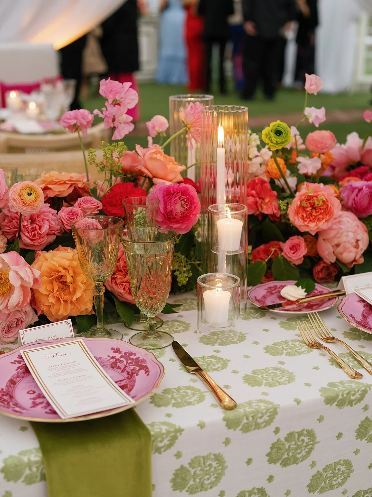  Close-up place setting with a pink patterned plate, gold flatware, and a coral floral centerpiece at Woodbine Mansion 