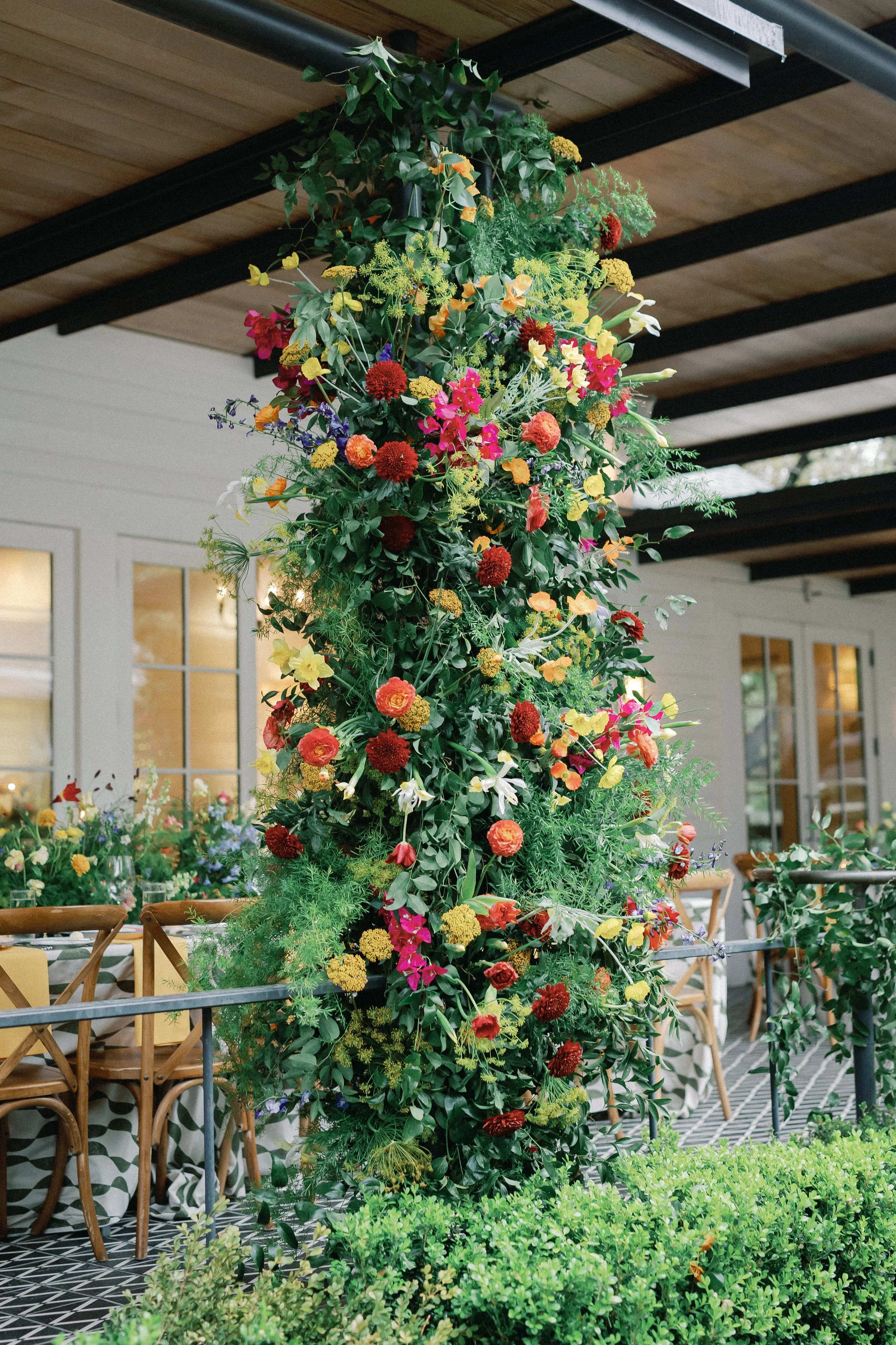  Tall cascading floral column in red, orange, and yellow against the farmhouse exterior at Mattie's 