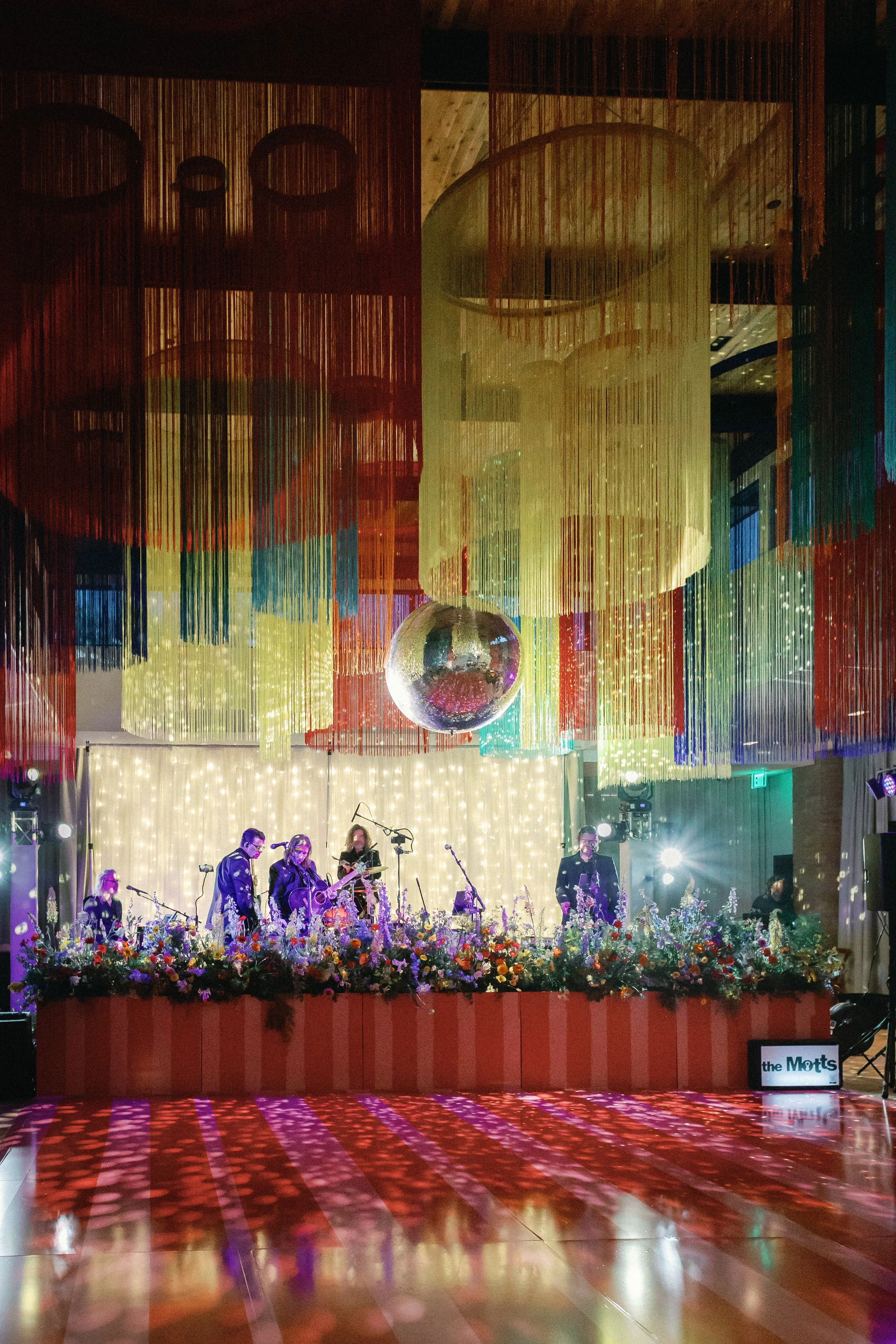  Wide view of the dance floor and band stage with a disco ball and colorful light projections at Mattie's 