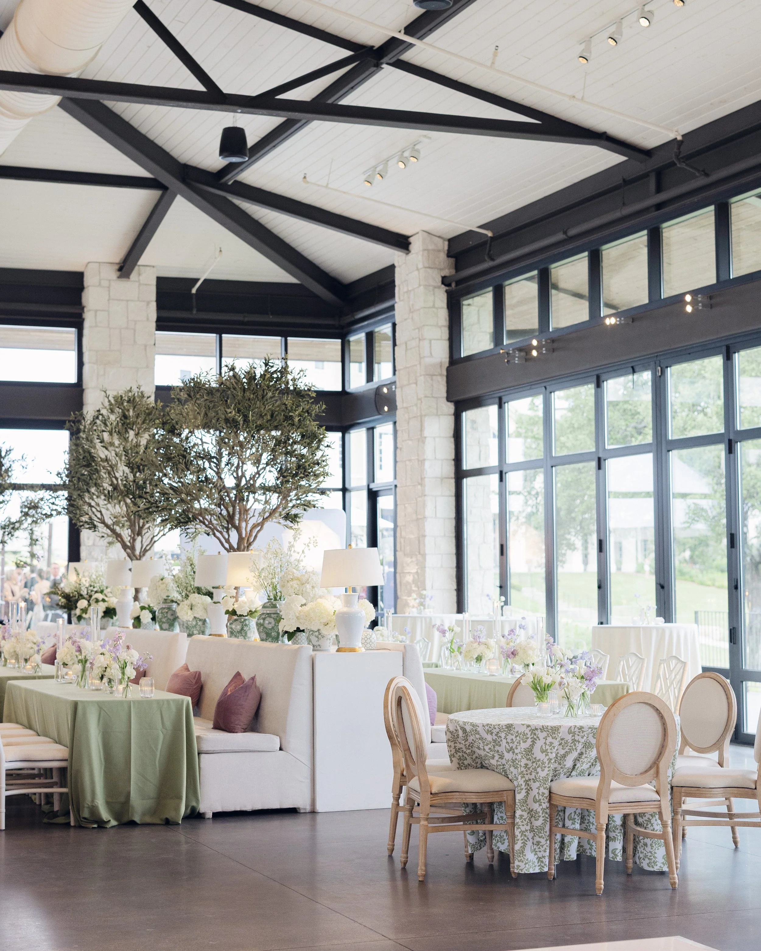  Wide view of Omni Barton Creek reception room with black beam ceiling, floor to ceiling windows, and floral centerpieces on round and long tables 