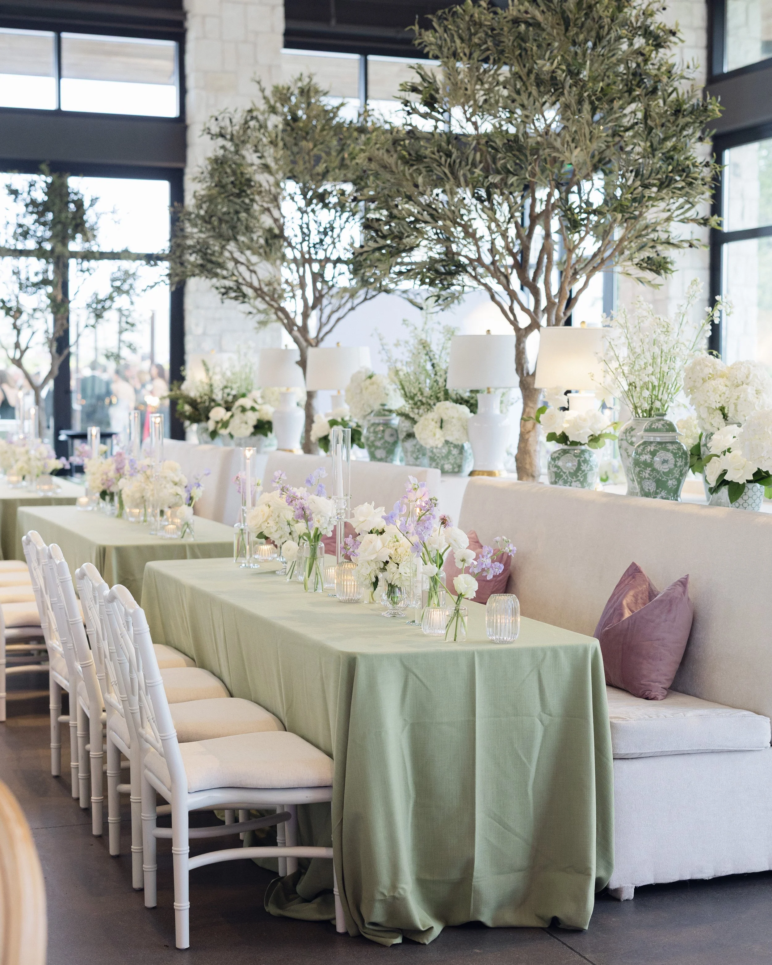 Long reception table lined with white chairs, faux olive trees, and sage green linen at Hill Country wedding venue 