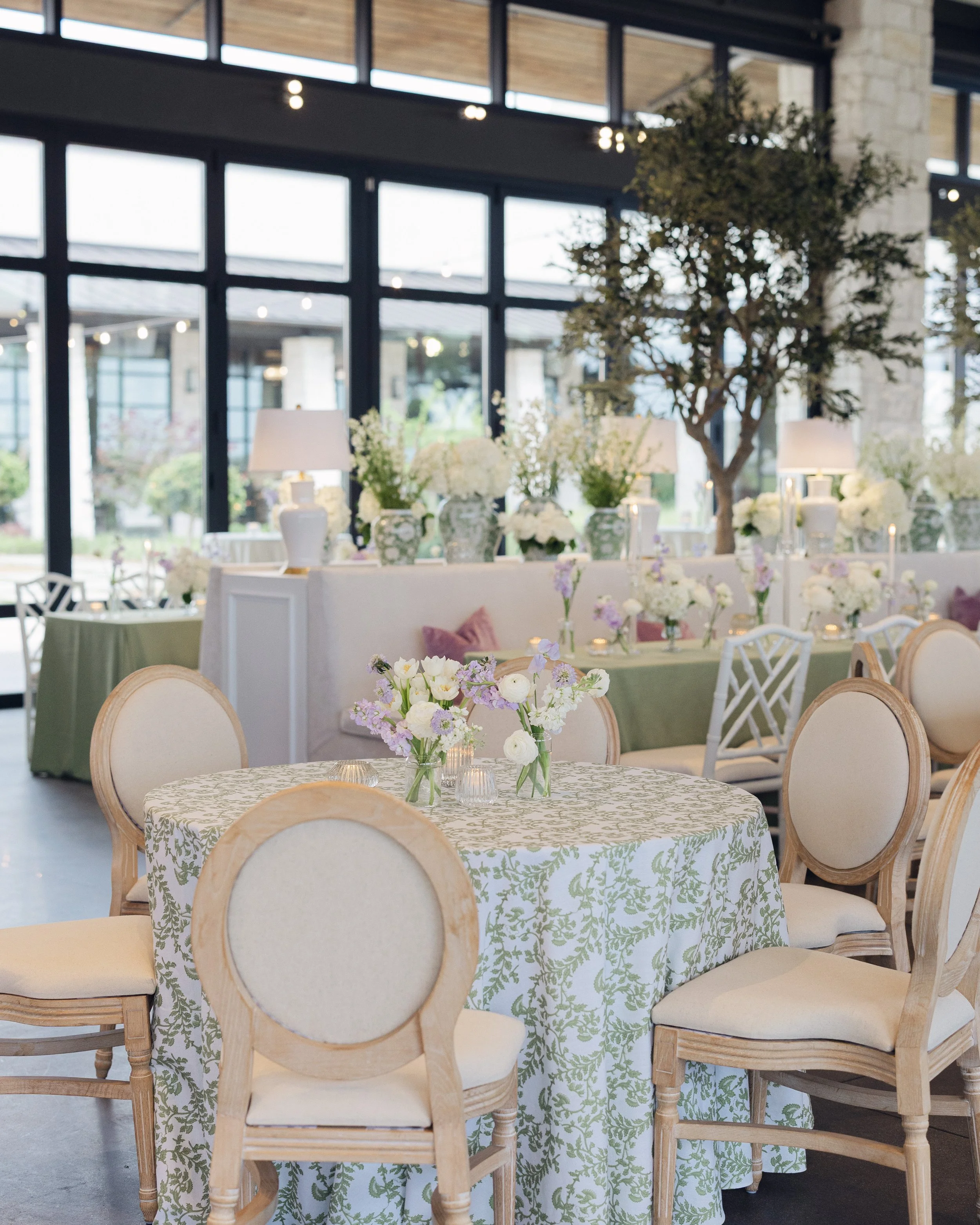  Round table with pale blue patterned linen, cream chairs, and lavender floral accents at Austin wedding reception 
