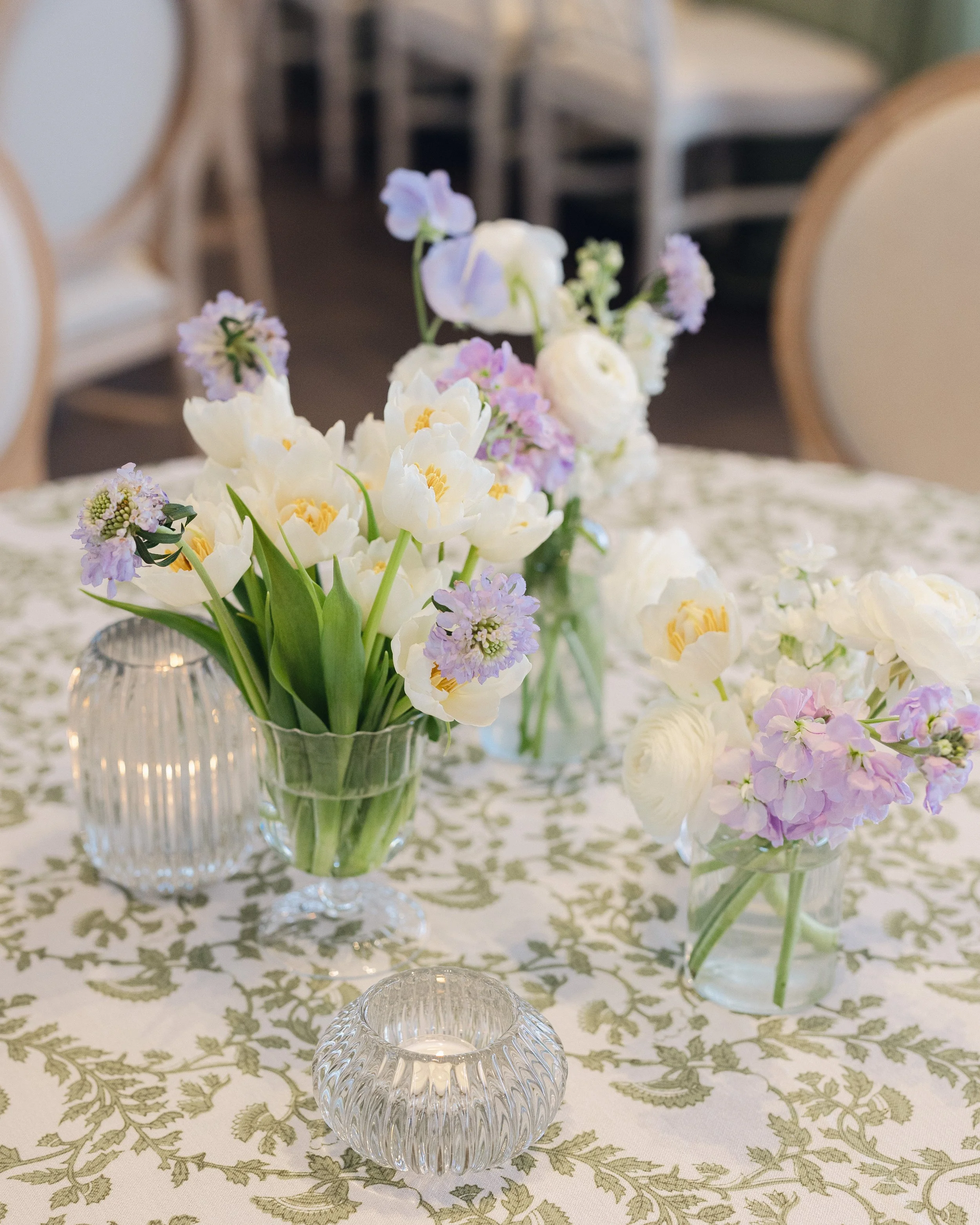  Close up centerpiece with lavender tulips, white sweet peas, and glass votive candles on patterned table linen 