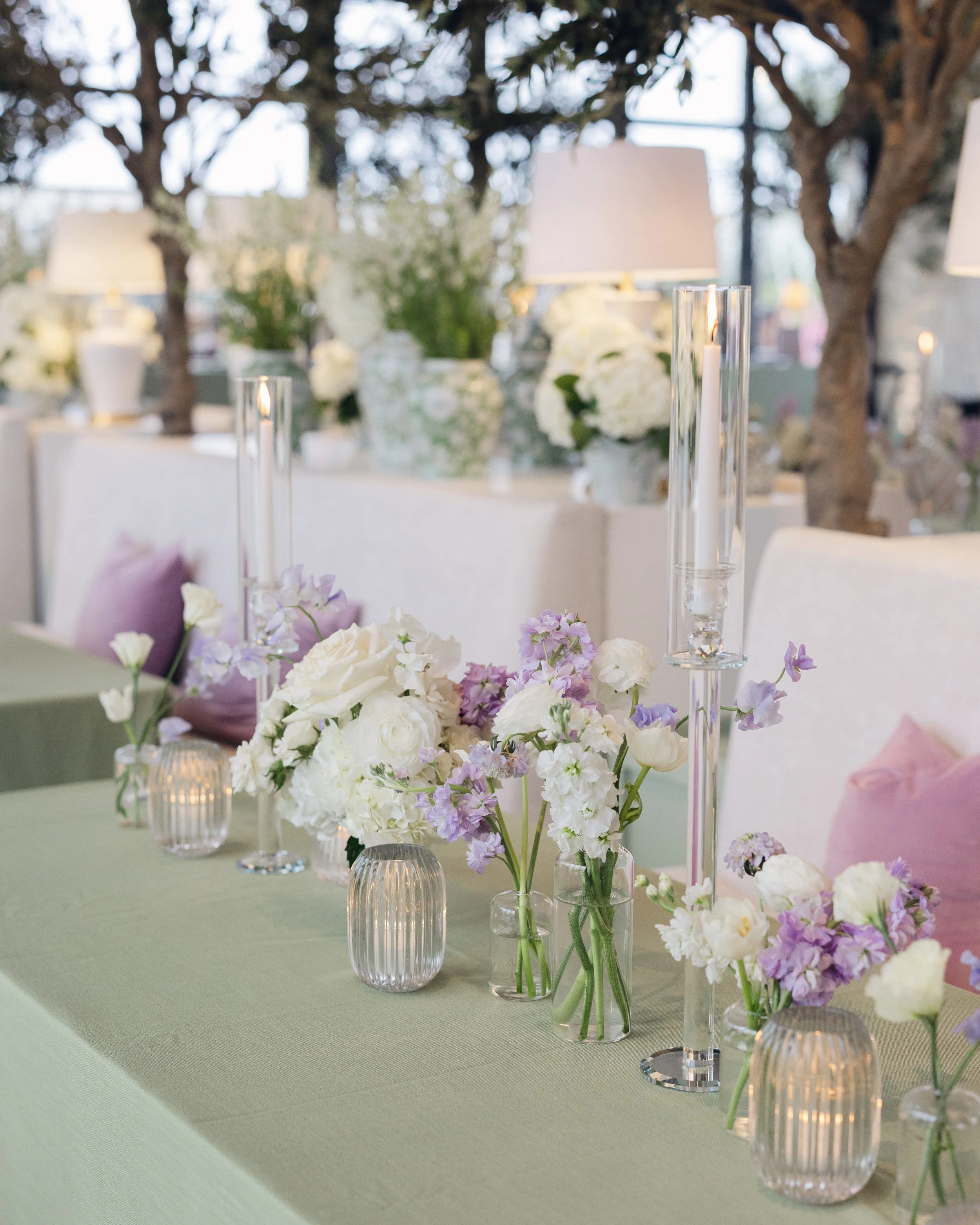  Reception table detail with white and lavender floral centerpiece and tall glass taper candle holders on sage green linen 