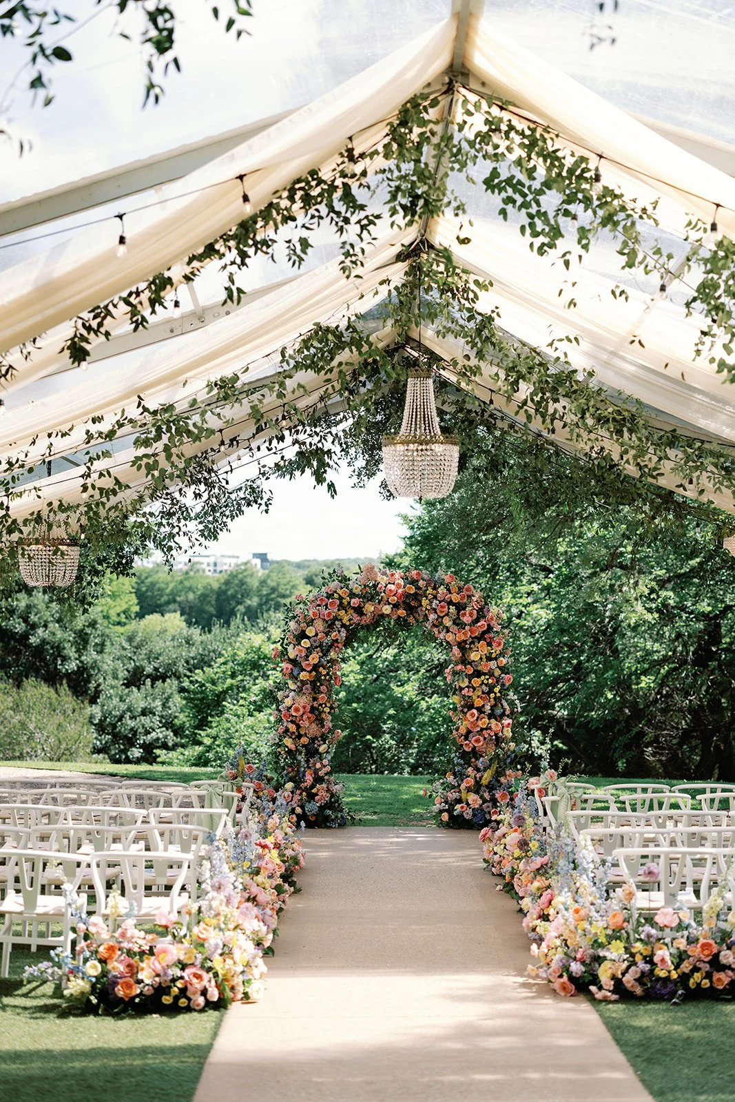  Wide view down the ceremony aisle under a clear tent with a crystal chandelier and floral arch at Four Seasons Austin 