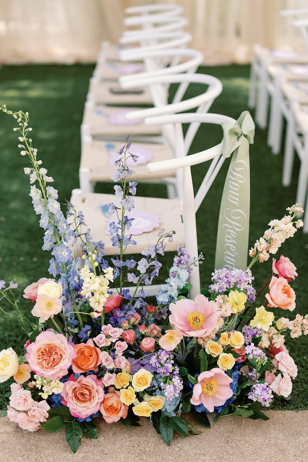  White ceremony chair with a colorful floral aisle arrangement in marigold, pink, and lavender at the base 