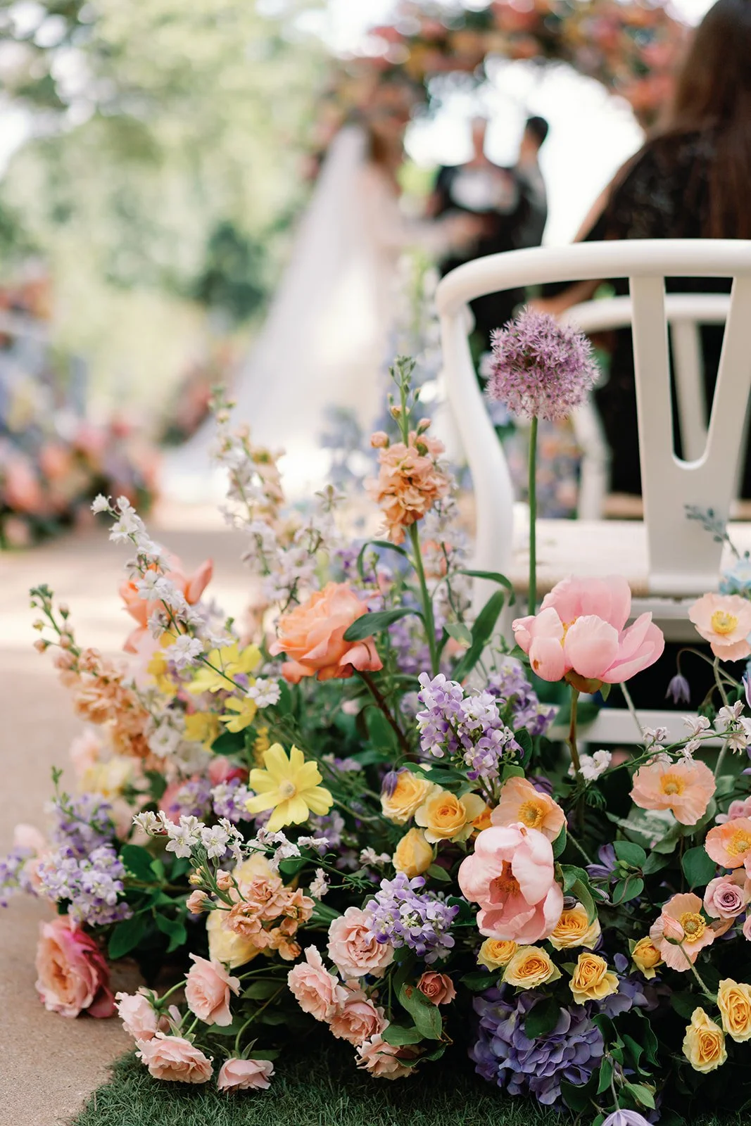  Close up of a floral aisle arrangement on a ceremony chair with white tent draping visible above 