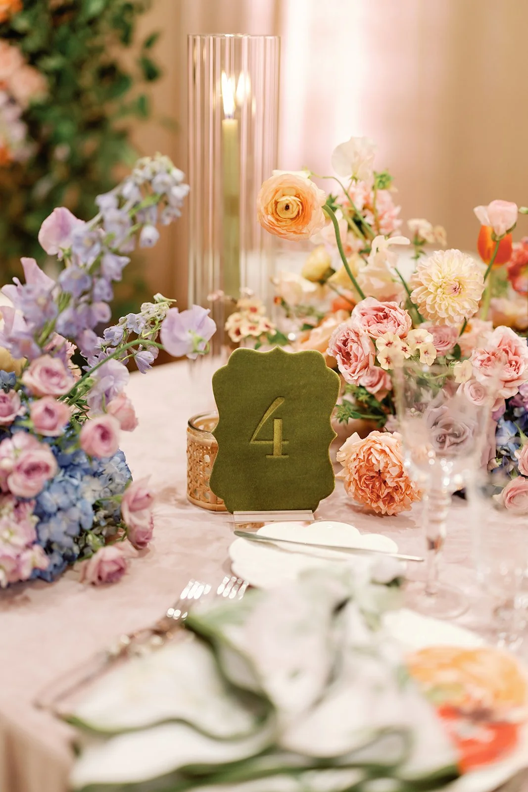  Reception table setting with green velvet table number, colorful centerpiece, and white place setting 