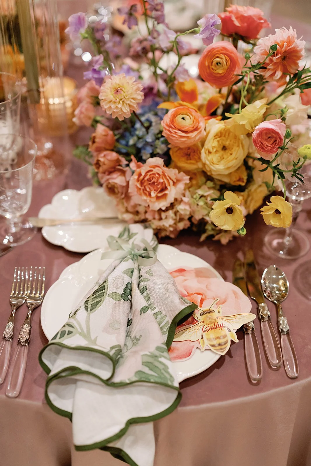  Reception table setting with mauve linen, floral centerpiece, and green edged napkin 