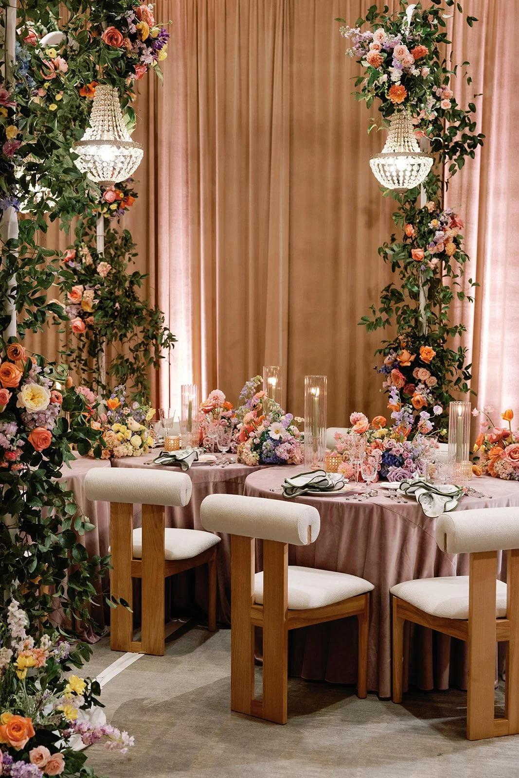  Long reception table lined with wood chairs beneath hanging floral and crystal chandelier installations 