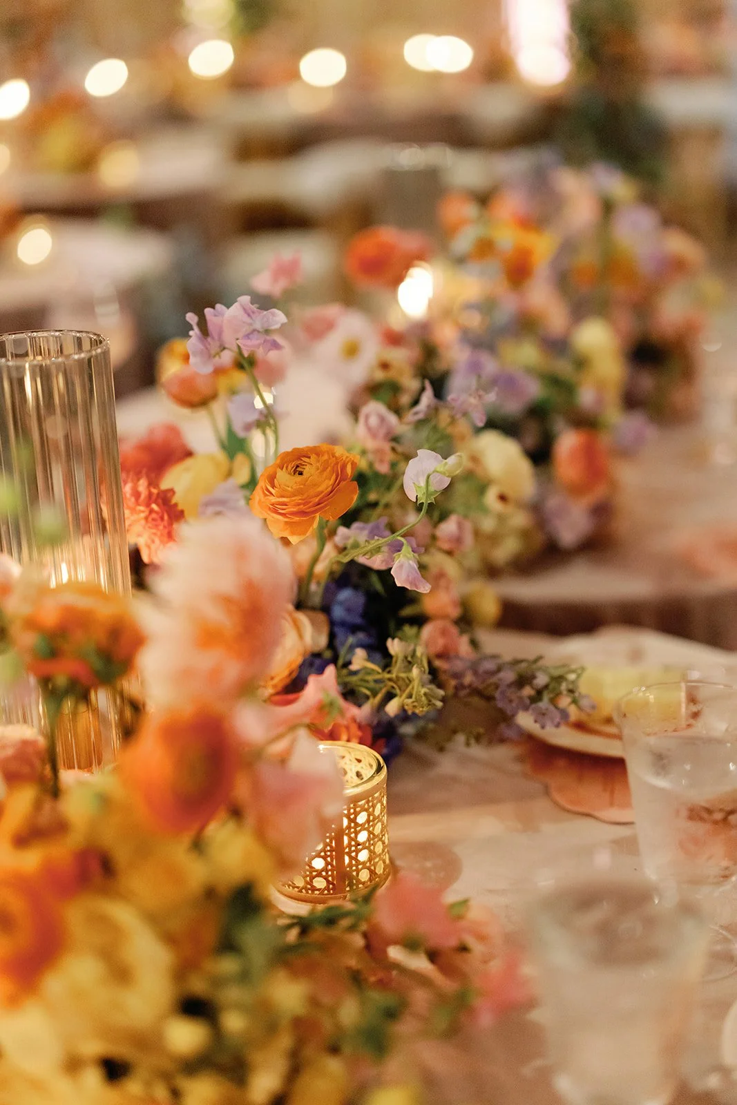  Reception table detail with tall taper candles, gold votives, and a blurred colorful centerpiece 