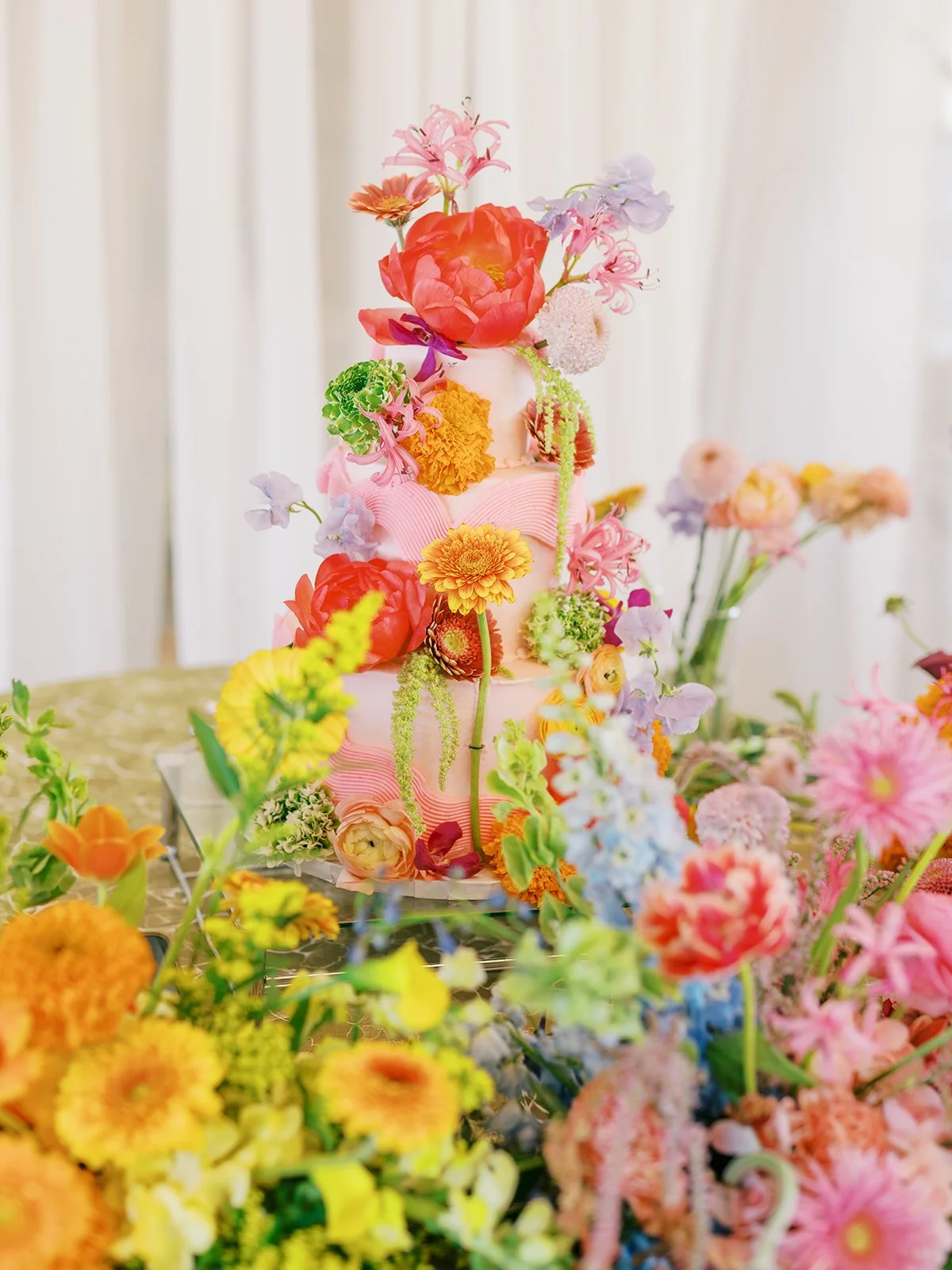  Wedding cake covered top to bottom in bright, colorful blooms on a green patterned tablecloth 