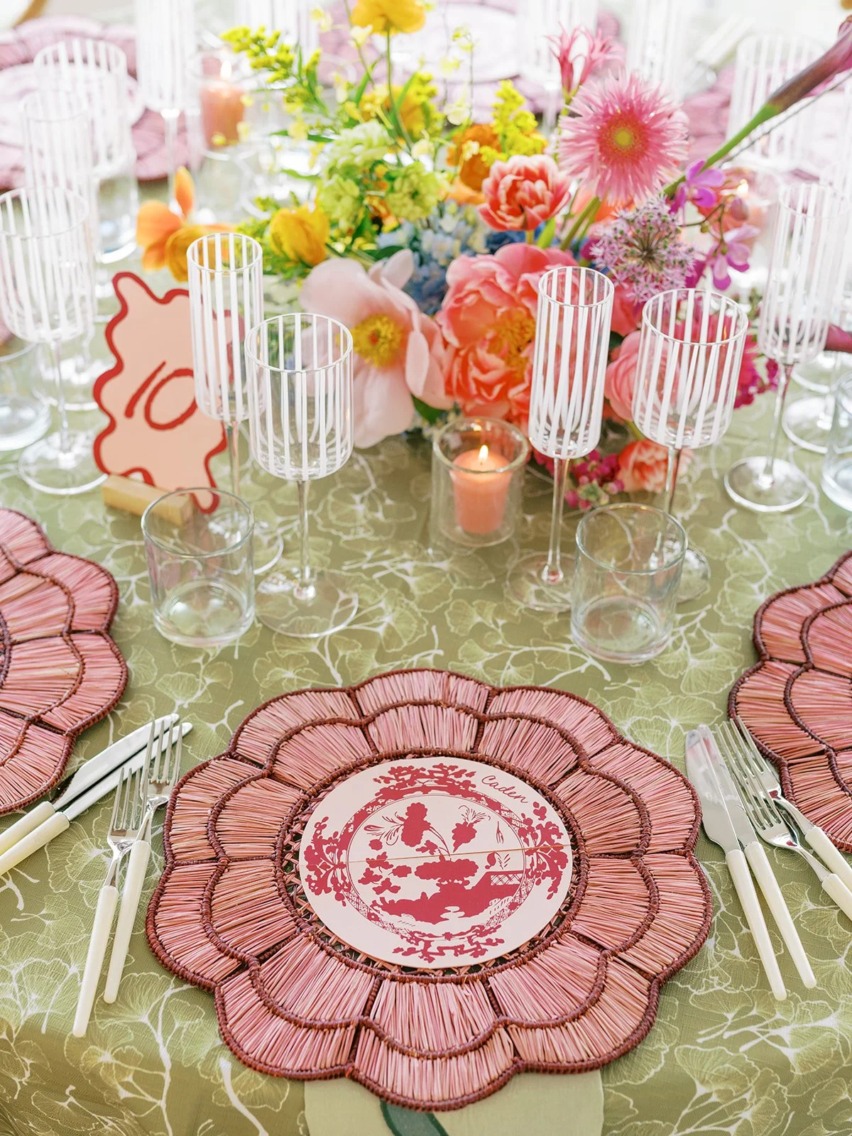 Table setting with a pink flower shaped charger, colorful table number, and taper candles 