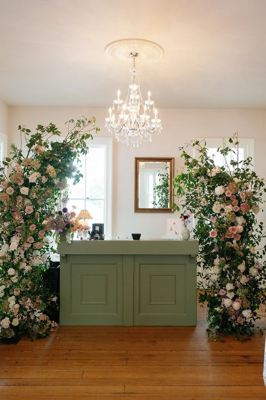  Tall garden rose arrangements framing a sage green bar beneath a crystal chandelier at The Allan House 
