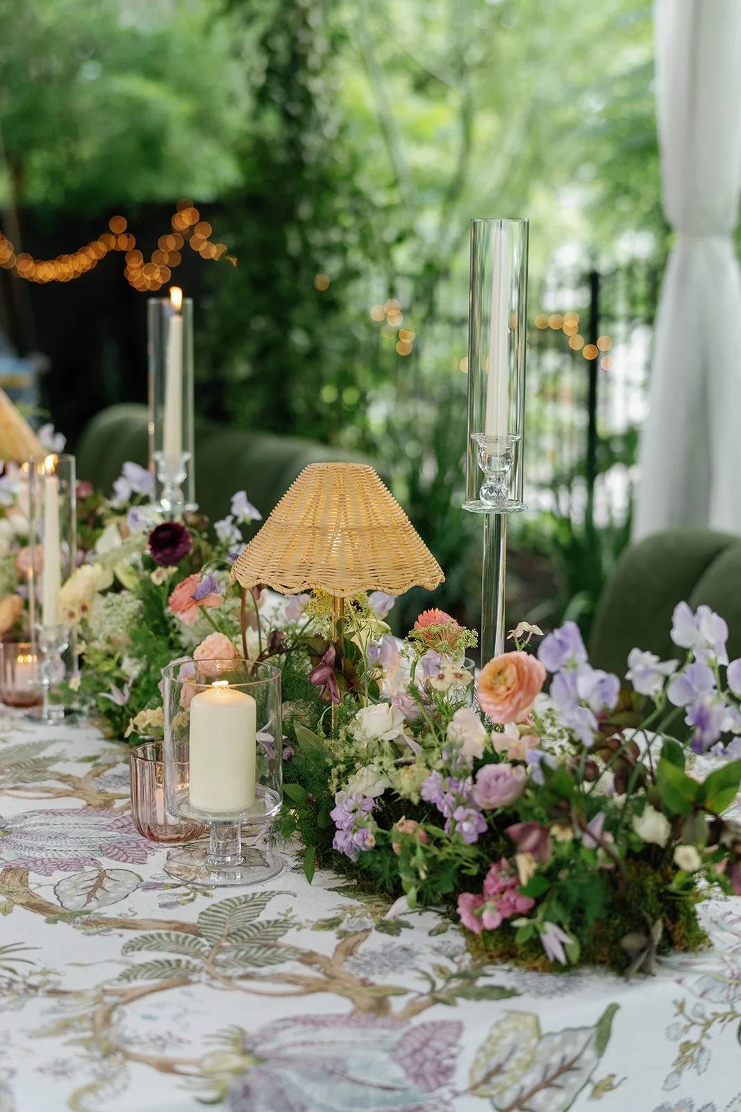  Peach ranunculus, blush roses and burgundy blooms beside a rattan lamp on a reception table at The Allan House 