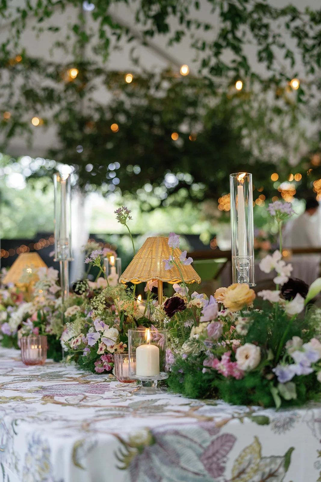  Low garden-style centerpiece with lavender and peach blooms and candles in glass hurricanes at The Allan House 