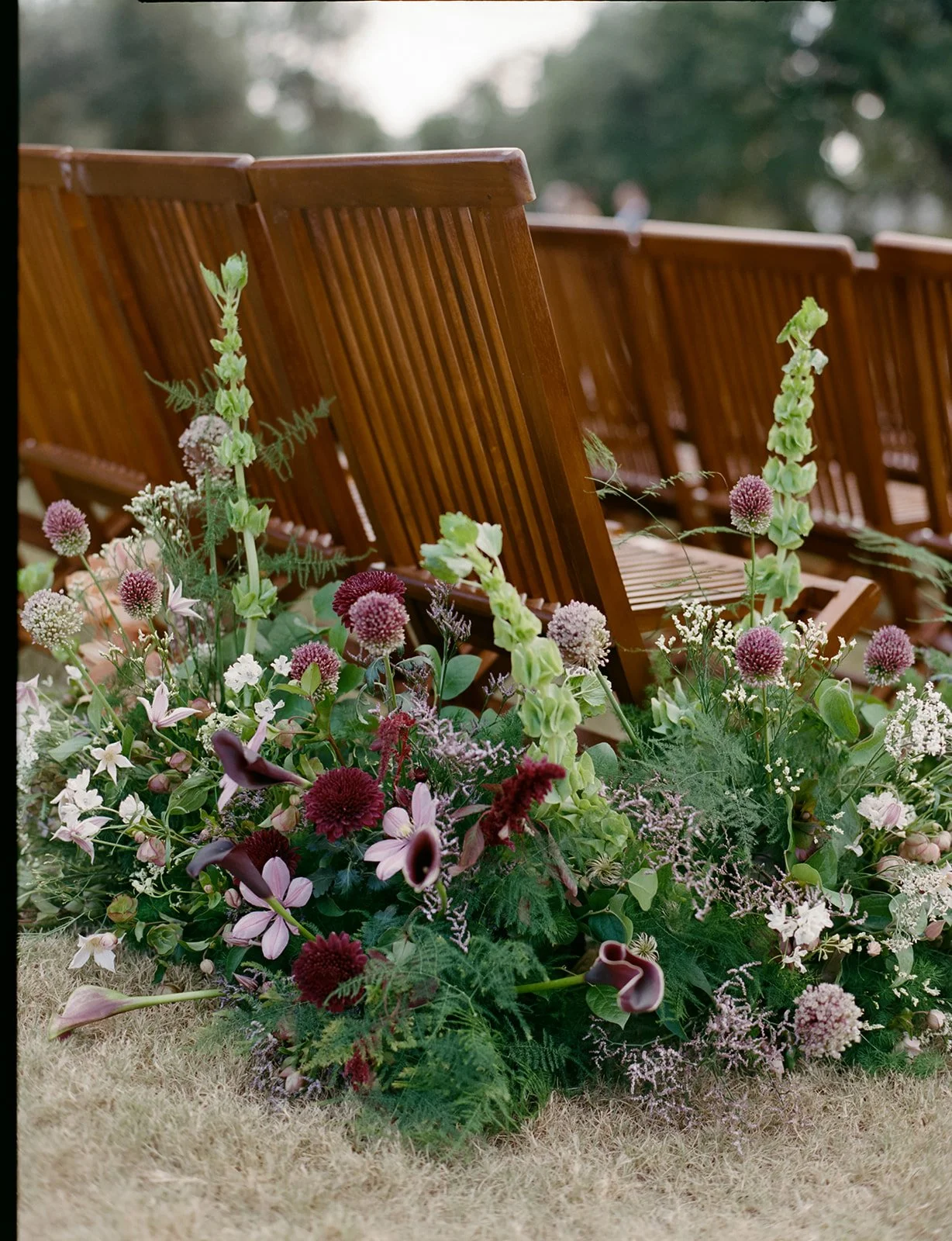  Moody ground-level aisle arrangement of burgundy dahlias, plum calla lilies and purple clematis at a Camp Lucy wedding 
