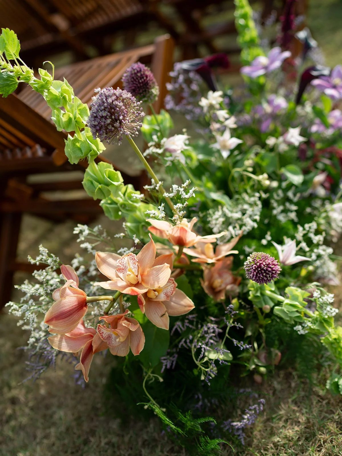  Garden-style ceremony florals with allium and bells of Ireland at the end of a row of wooden chairs at Camp Lucy 