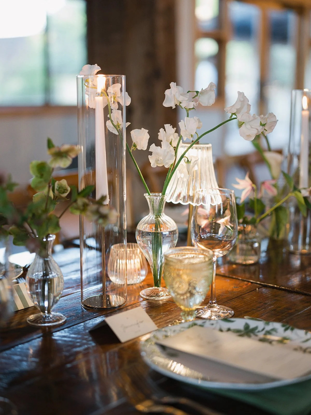  White sweet peas in a glass bud vase beside a taper candle and ribbed glass lamp at a Camp Lucy reception, designed by Remi + Gold 