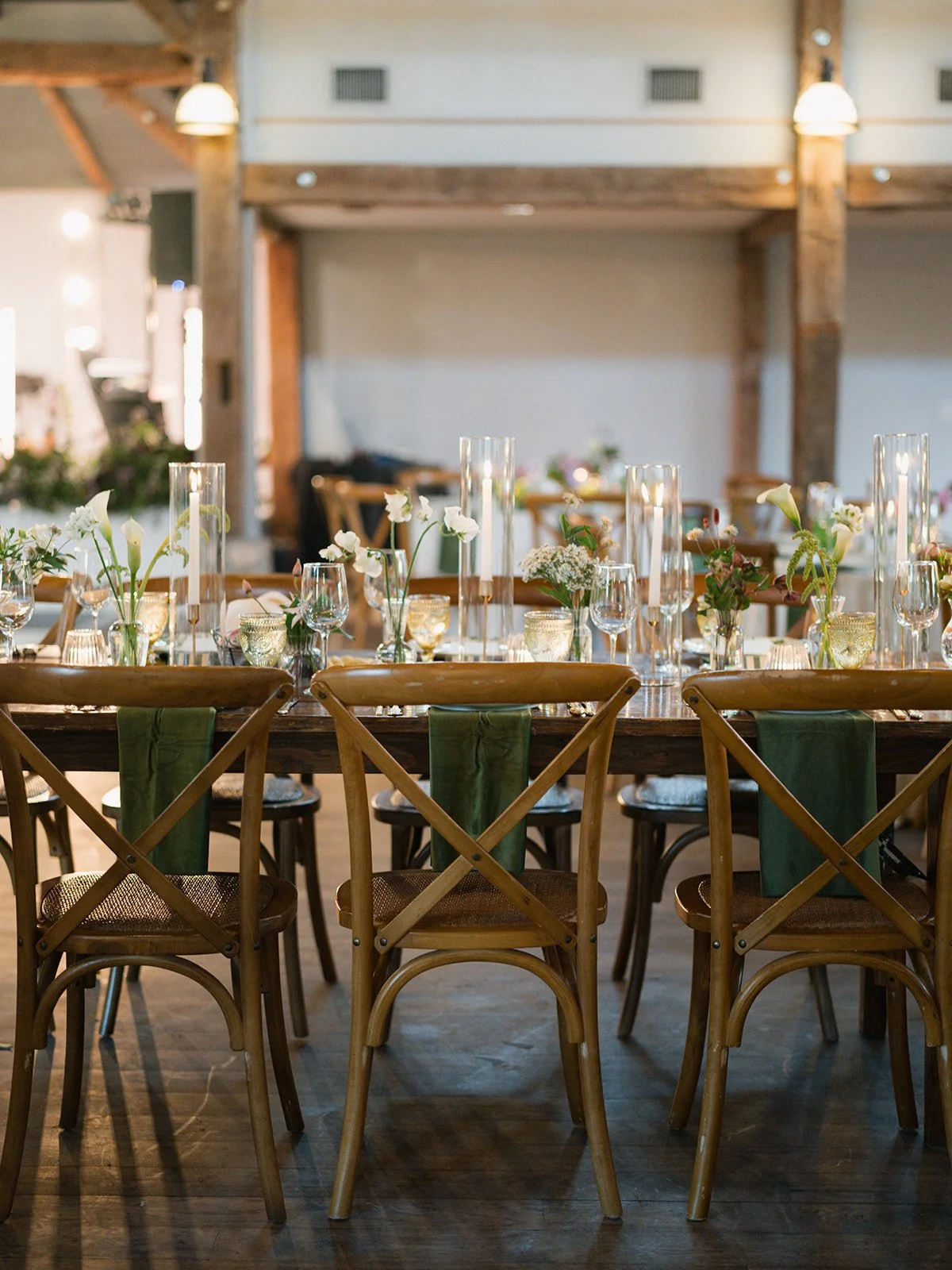  Long wooden farm table with taper candles, calla lily bud vases and forest green napkins at a Camp Lucy wedding reception 