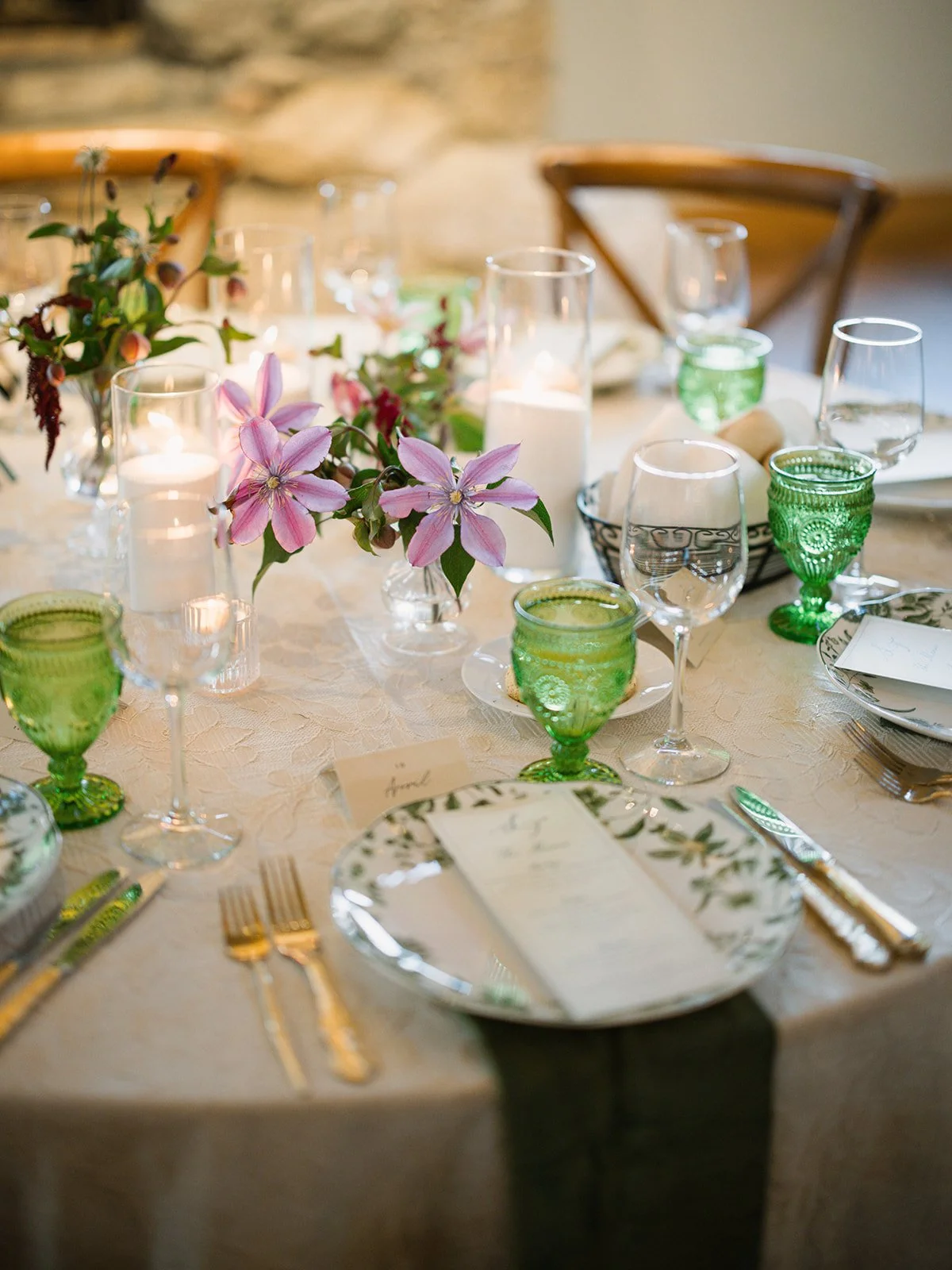  Pink clematis bud vases, pillar candles and green goblets on a lace-covered round reception table at Camp Lucy 