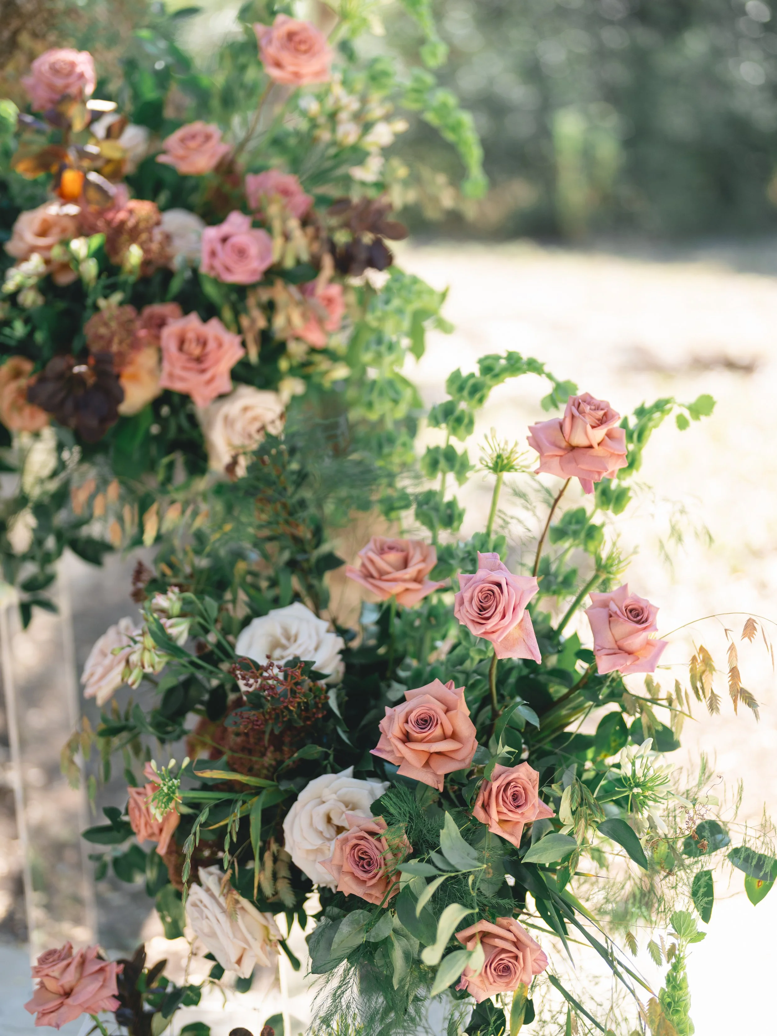  Close-up of mauve, blush and ivory roses with bells of Ireland and wispy grasses in a ceremony installation at The Addison Grove 