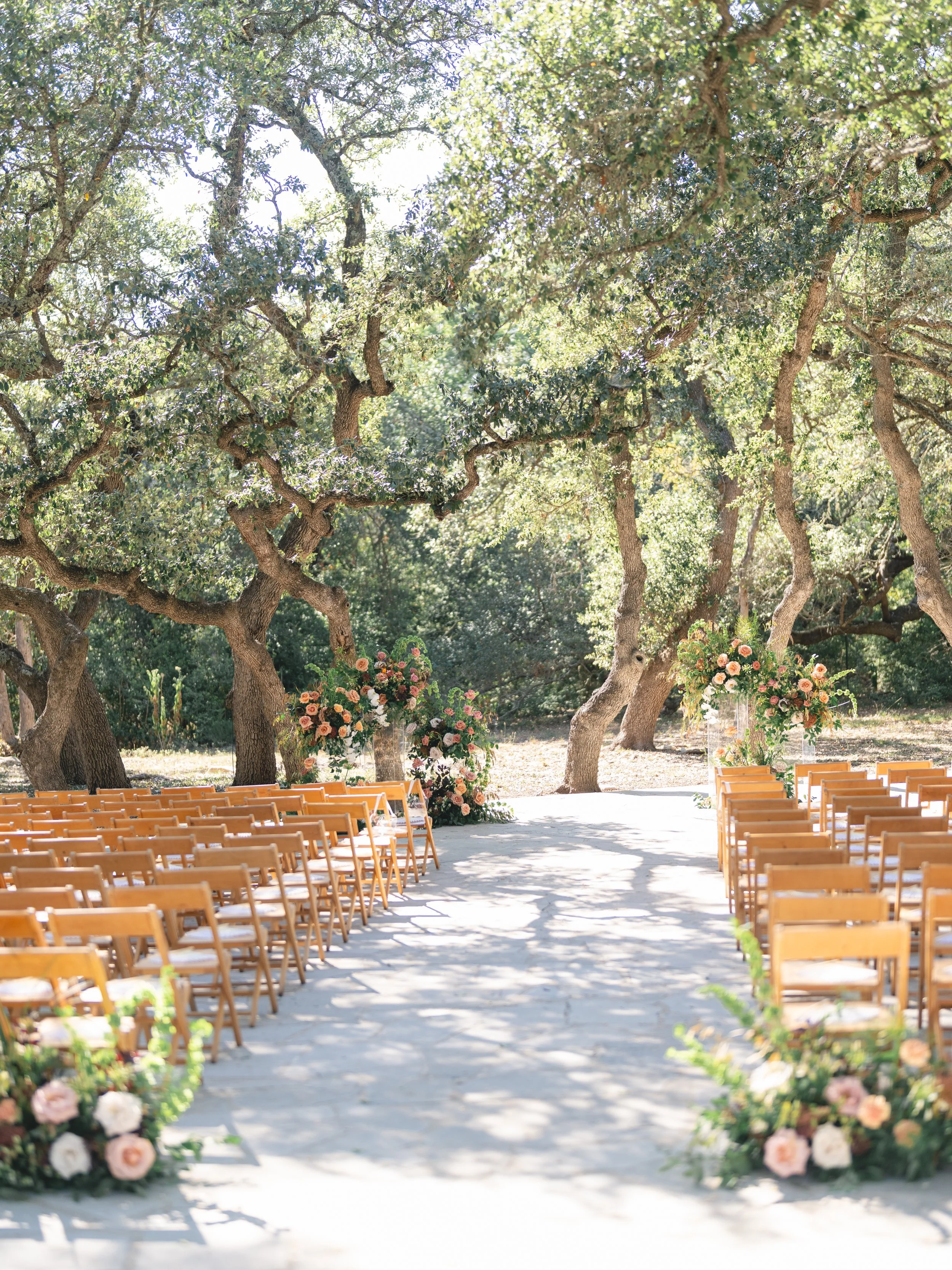  Outdoor wedding ceremony in the grove at The Addison Grove, with ground-level aisle florals and floral installations framing the altar beneath twisting trees 