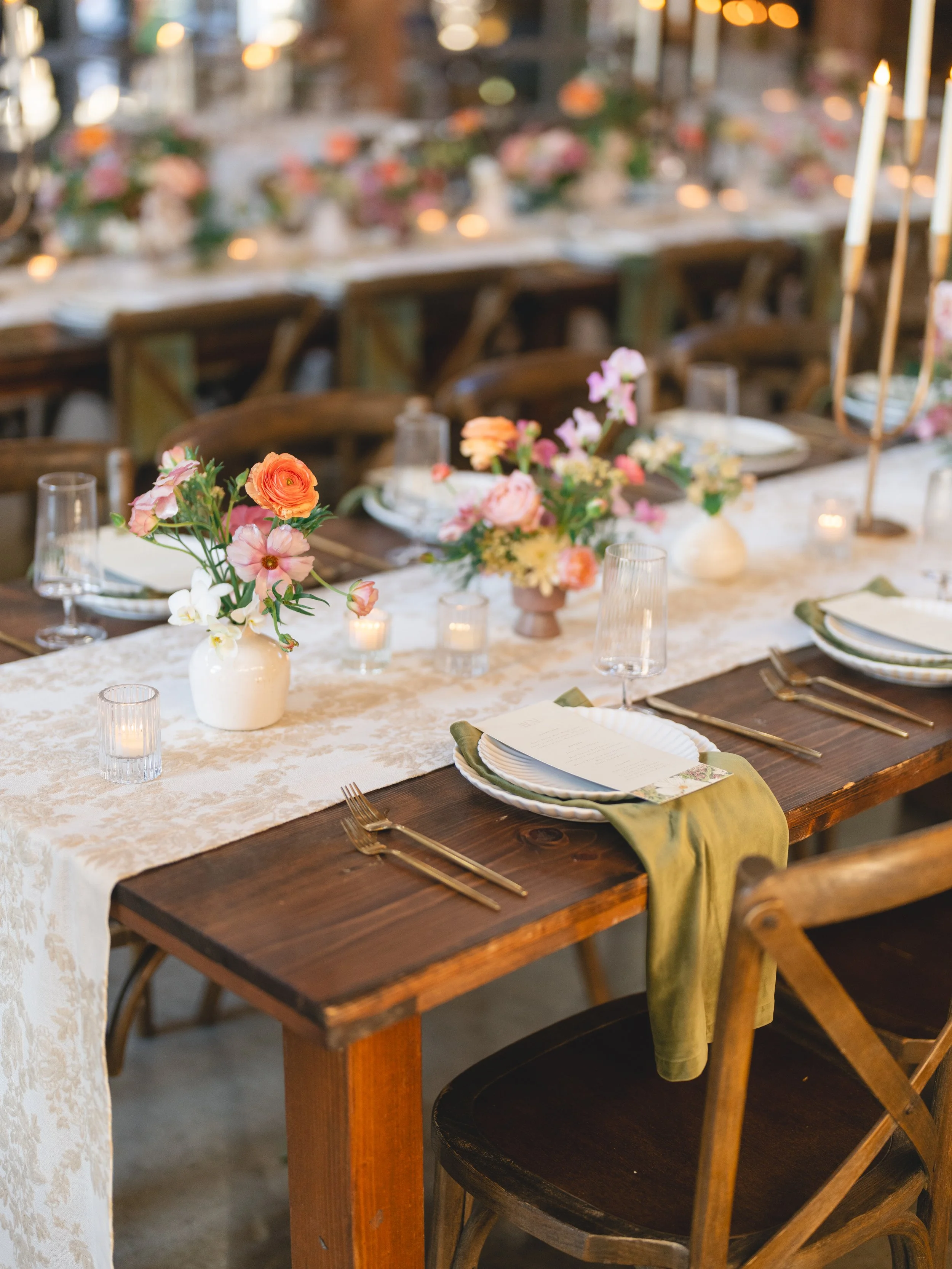  Close-up of a place setting with bud vases of orange ranunculus, cosmos and sweet peas on a farm table at The Addison Grove 