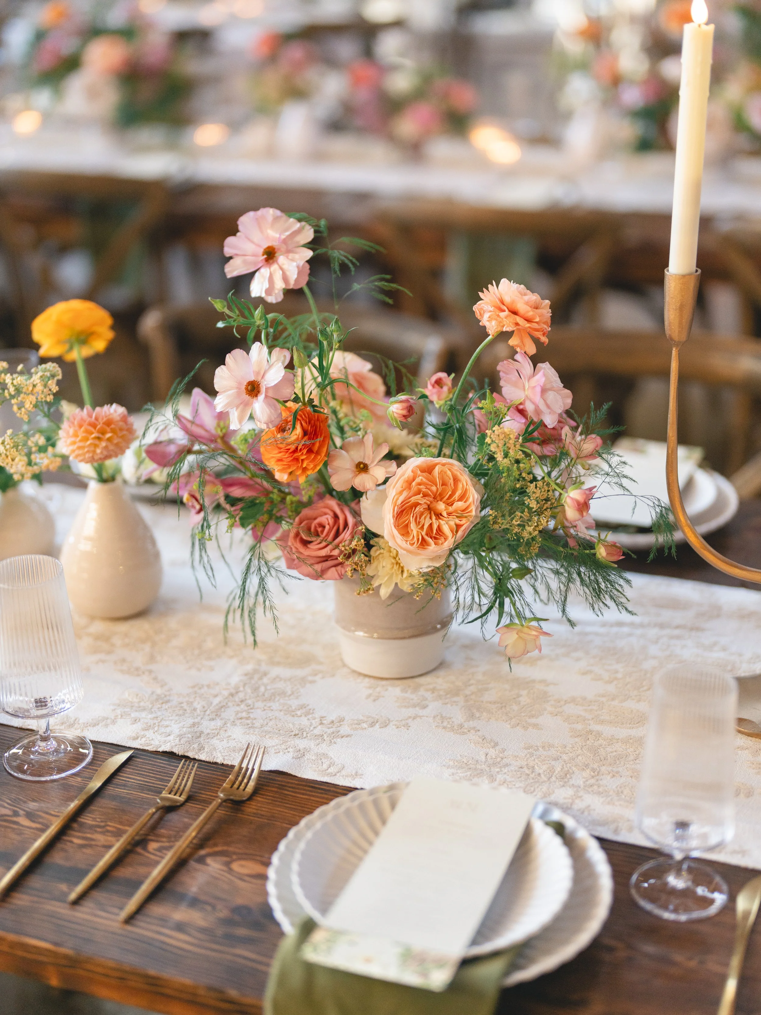  Close-up of a low centerpiece with a peach garden rose, orange ranunculus, cosmos and yarrow in a ceramic vessel at The Addison Grove 