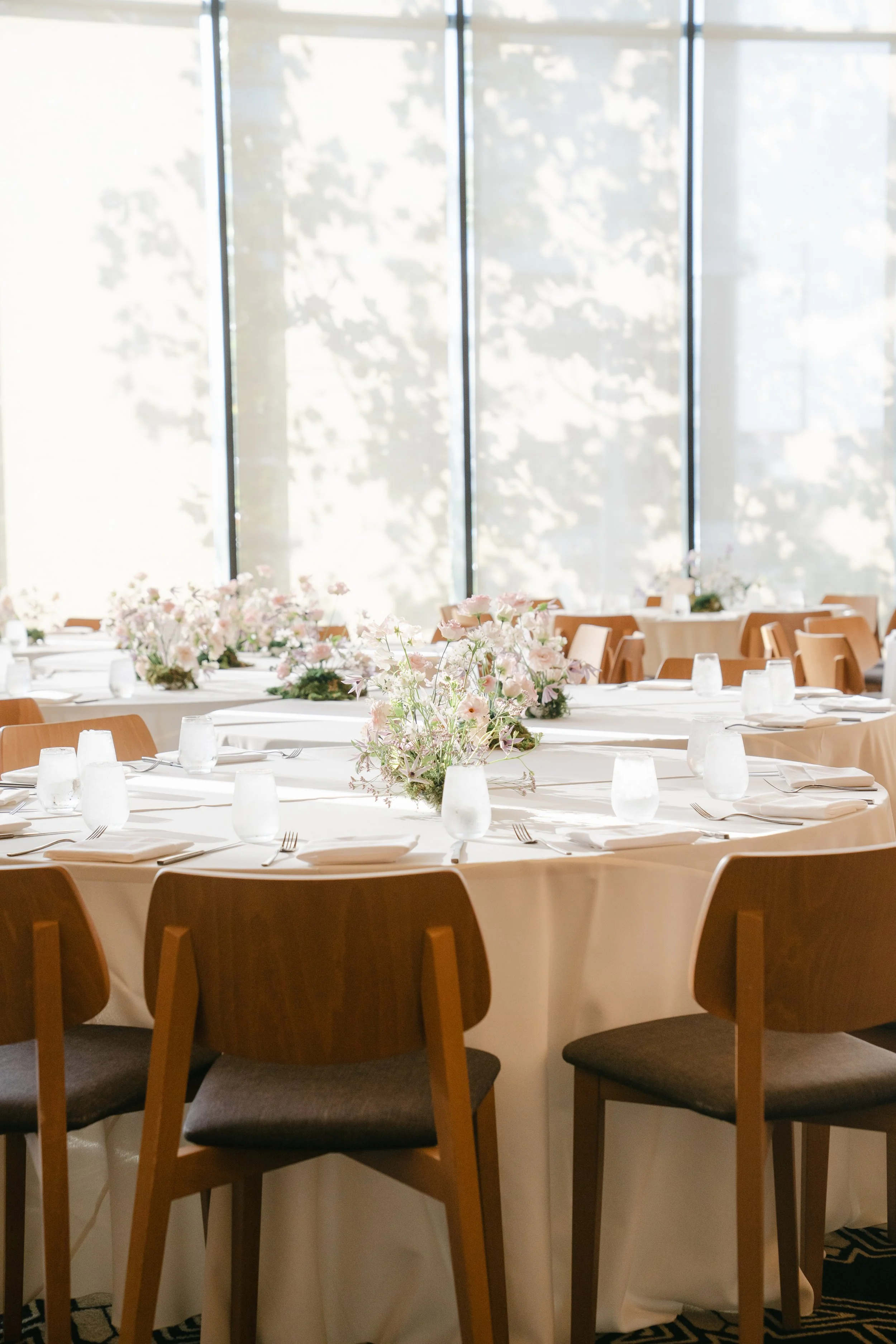 Airy blush and lavender centerpieces on round tables in front of sunlit windows at Austin Proper Hotel, designed by Remi + Gold