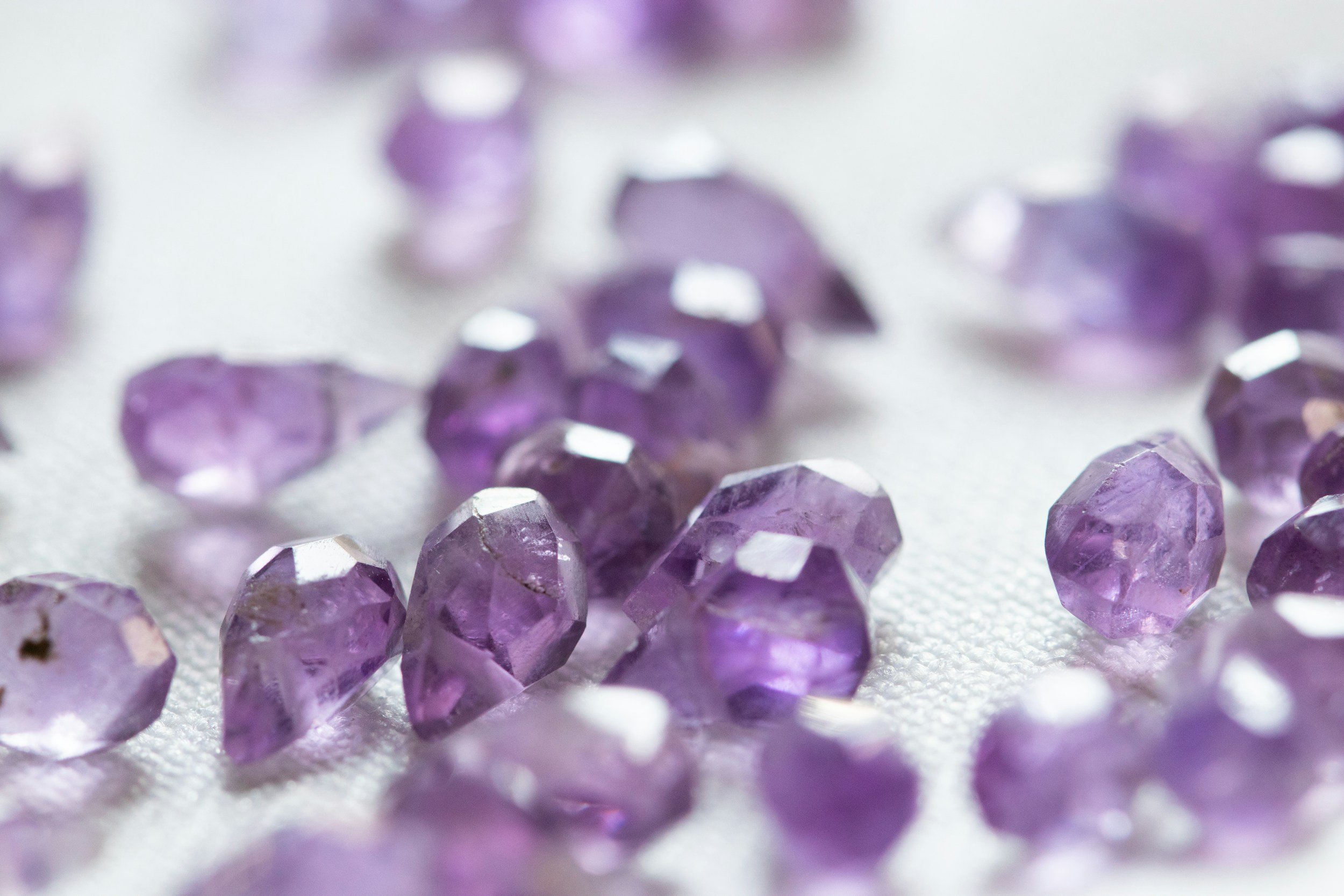 Close-up of small, faceted, purple gemstones scattered on a white surface.