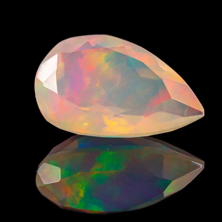 A teardrop-shaped opal gemstone with iridescent colors on a black reflective surface.