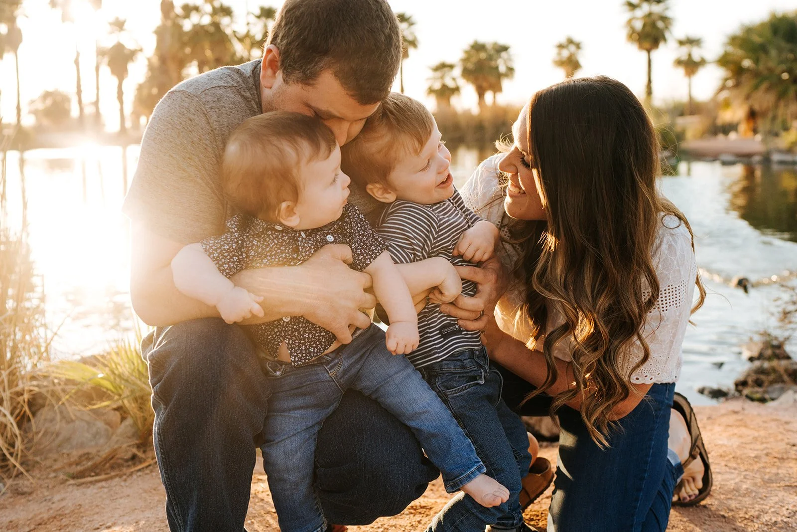Family enjoying a playful moment by the water at sunset, with palm trees in the background.