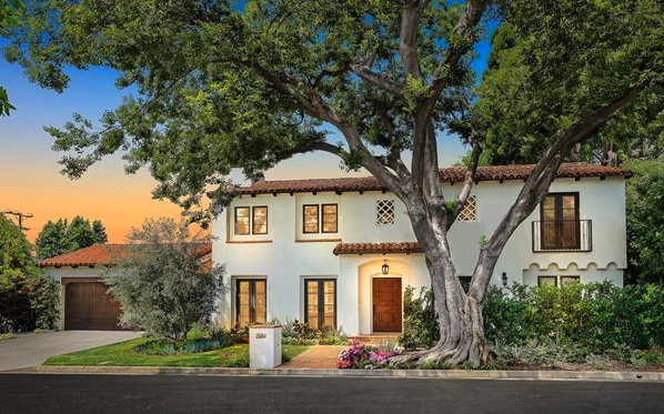 Front view of a two-story house with white exterior, brown roof tiles, and a large tree in the front yard.