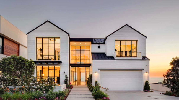 Modern two-story house with large windows, a white exterior, and a landscaped front yard during sunset.