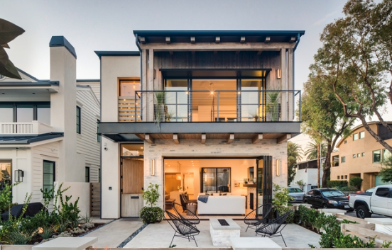Modern two-story house with a balcony, large windows, outdoor seating area, and landscaped front yard.