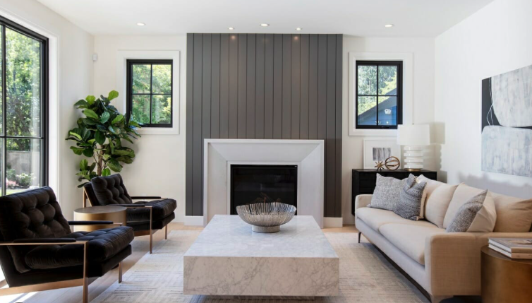 Modern living room with white sofa, black armchairs, marble coffee table, fireplace, potted plant, and large windows
