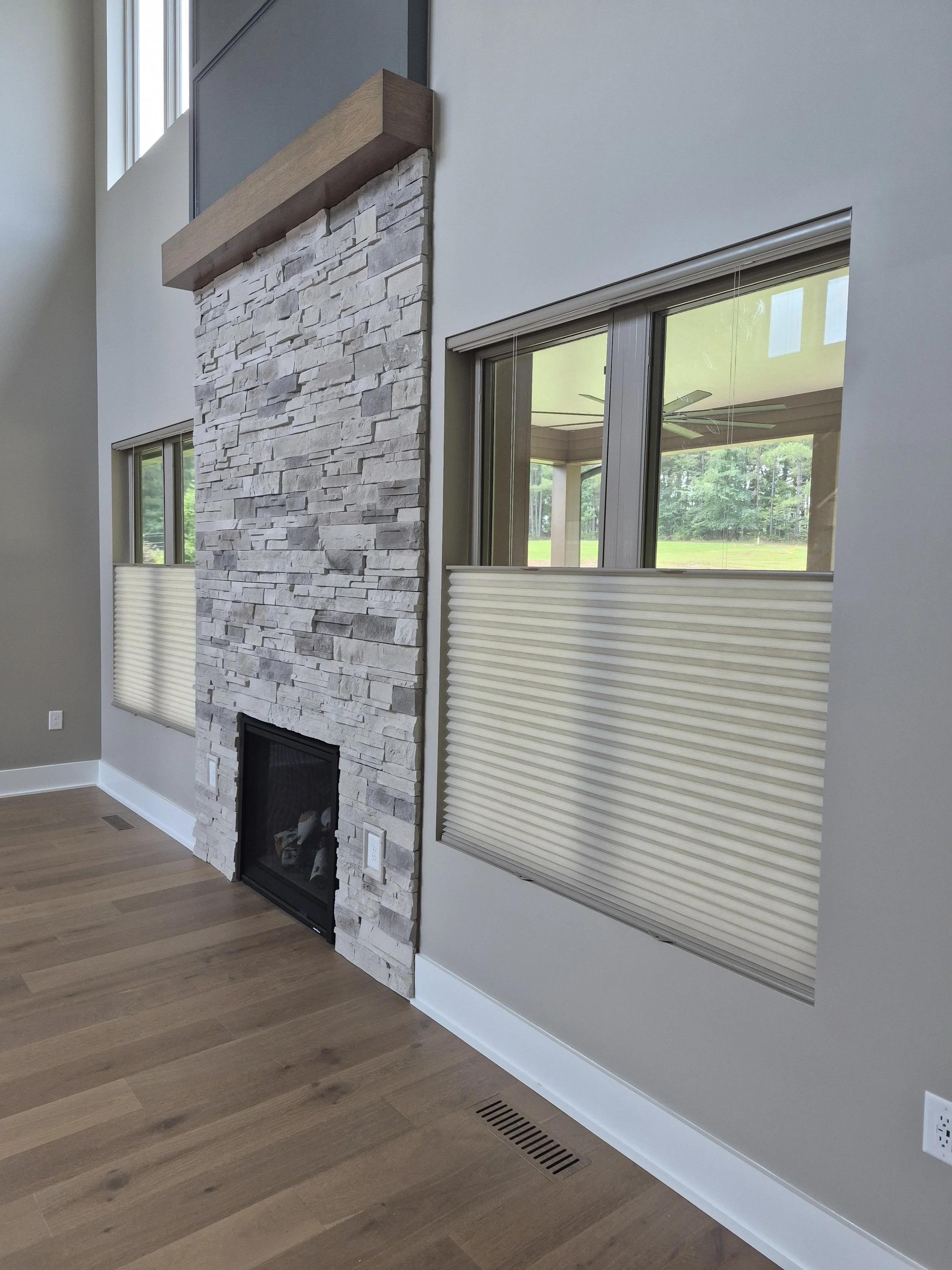 Top-down bottom-up honeycomb shades lowered halfway on double windows in a living room with a stone fireplace.