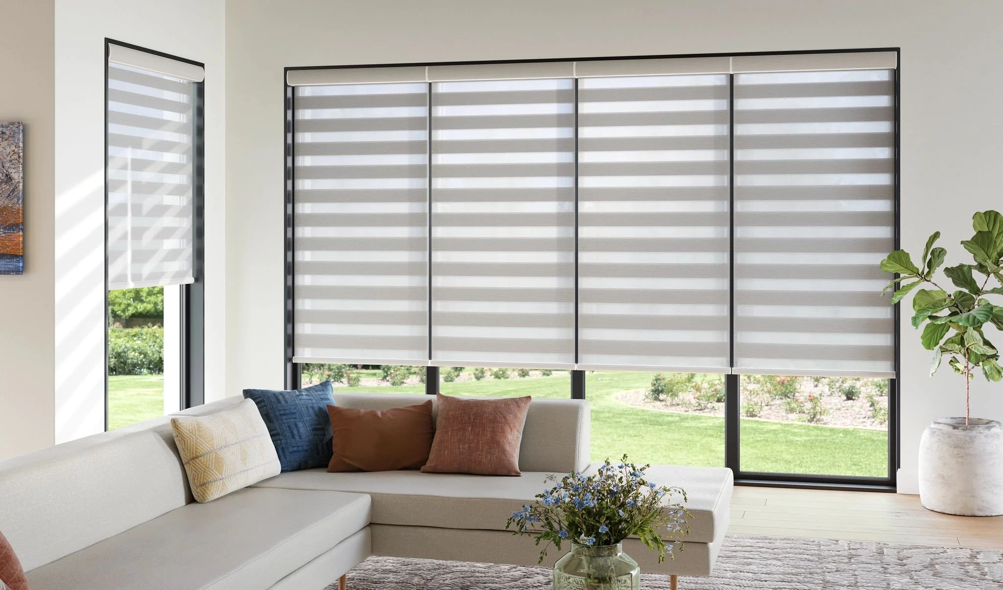 White banded shades covering expansive windows in a light-filled living room behind a sectional sofa with colorful accent pillows.