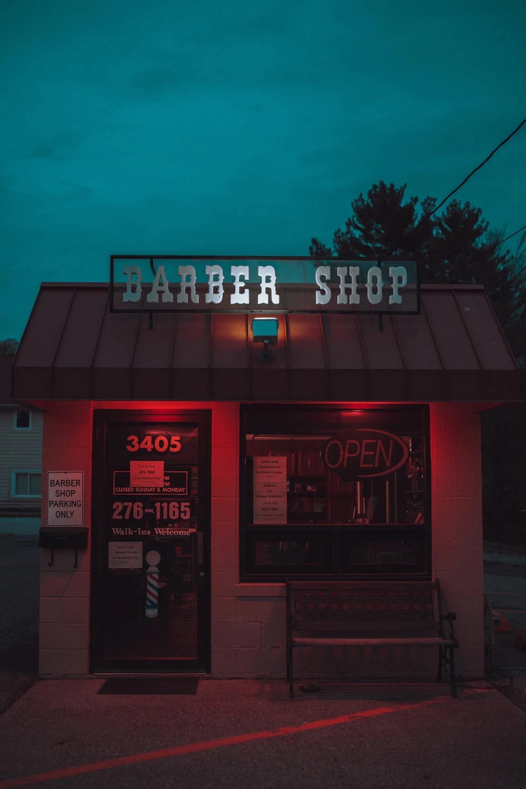 Nighttime photo of a small barber shop building with illuminated 'OPEN' sign, red neon lighting, and a 'Barber Shop' sign on top.