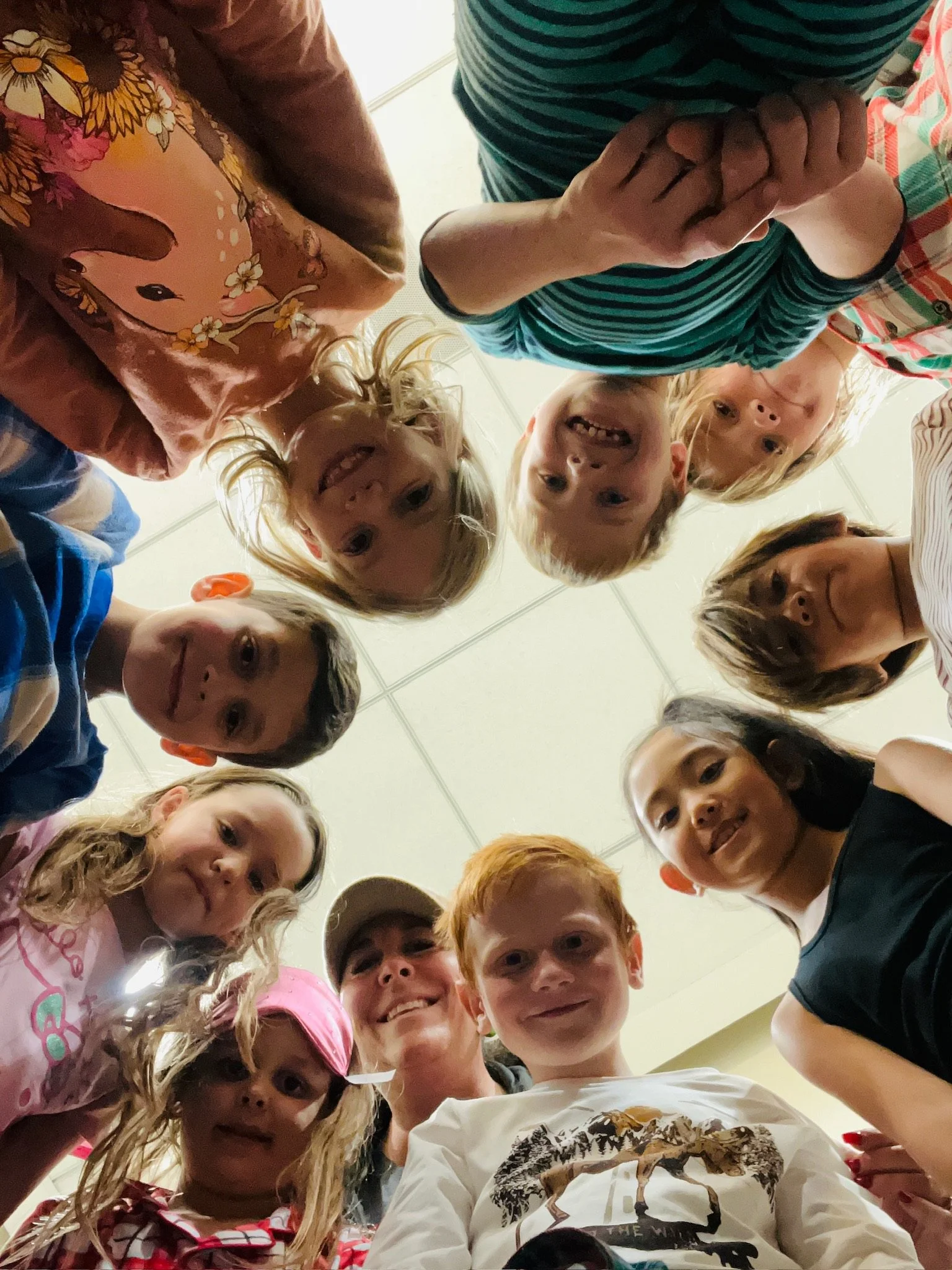 A group of children and an adult looking down at the camera, forming a circle and smiling.