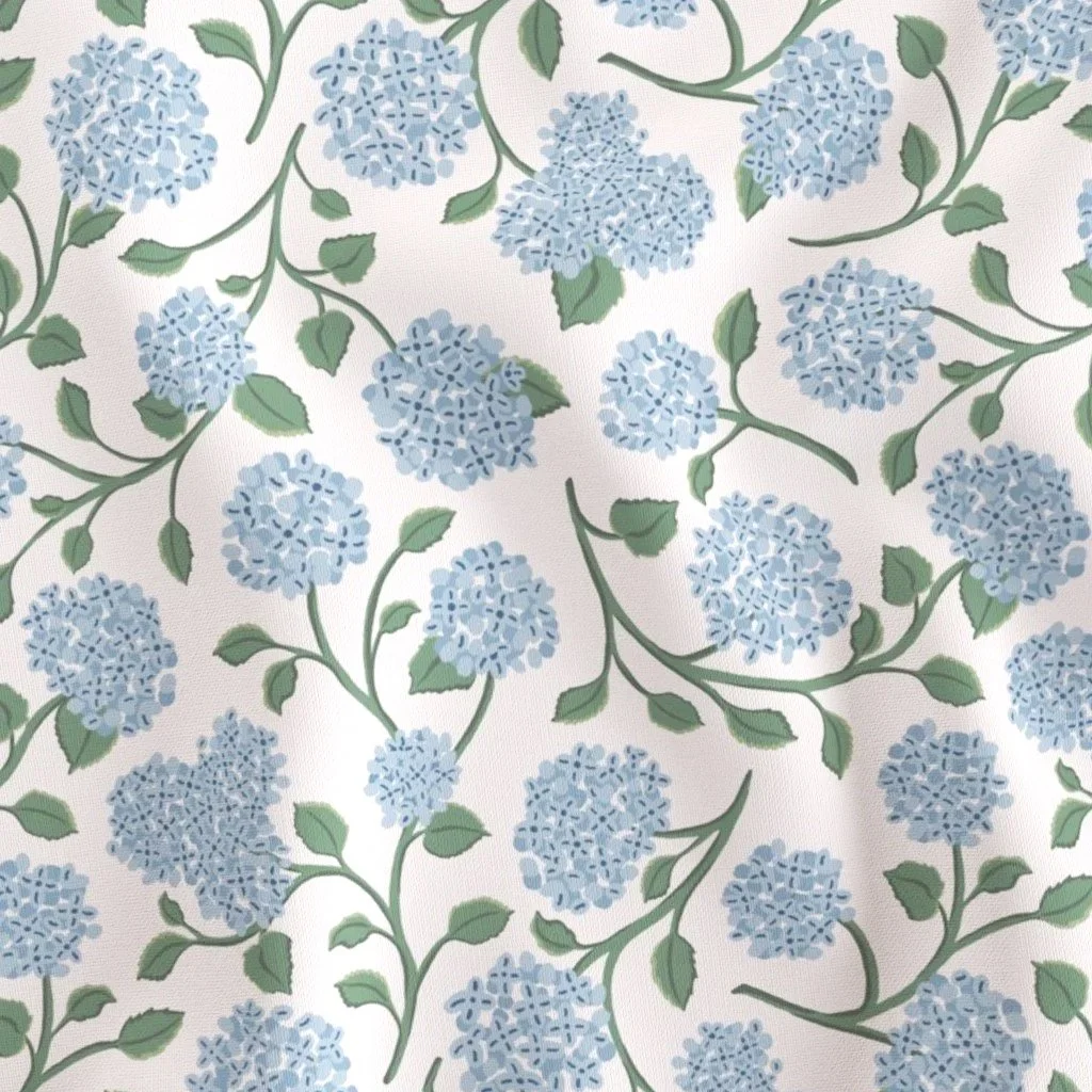 fabric surface pattern design with a classic heritage and cottagecore soft style featuring soft blue hydrangea floral clusters and green leaves on a cream background. The fabric texture is subtly visible, suggesting a cozy bedroom or nursery setting.