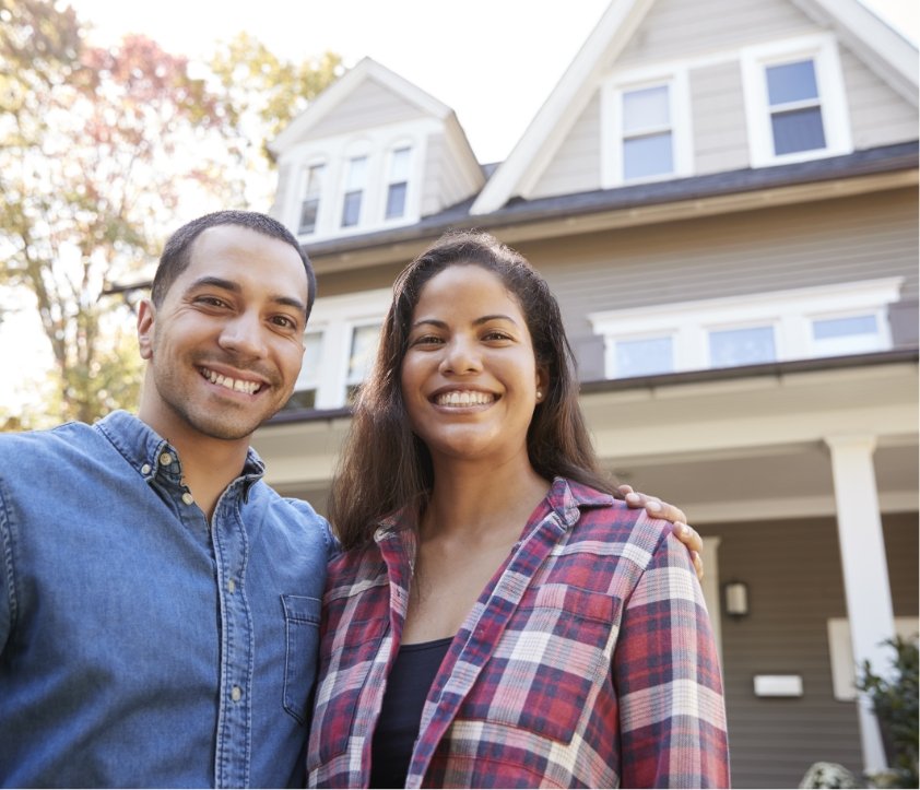 A hispanic couple standing in front of their first home.