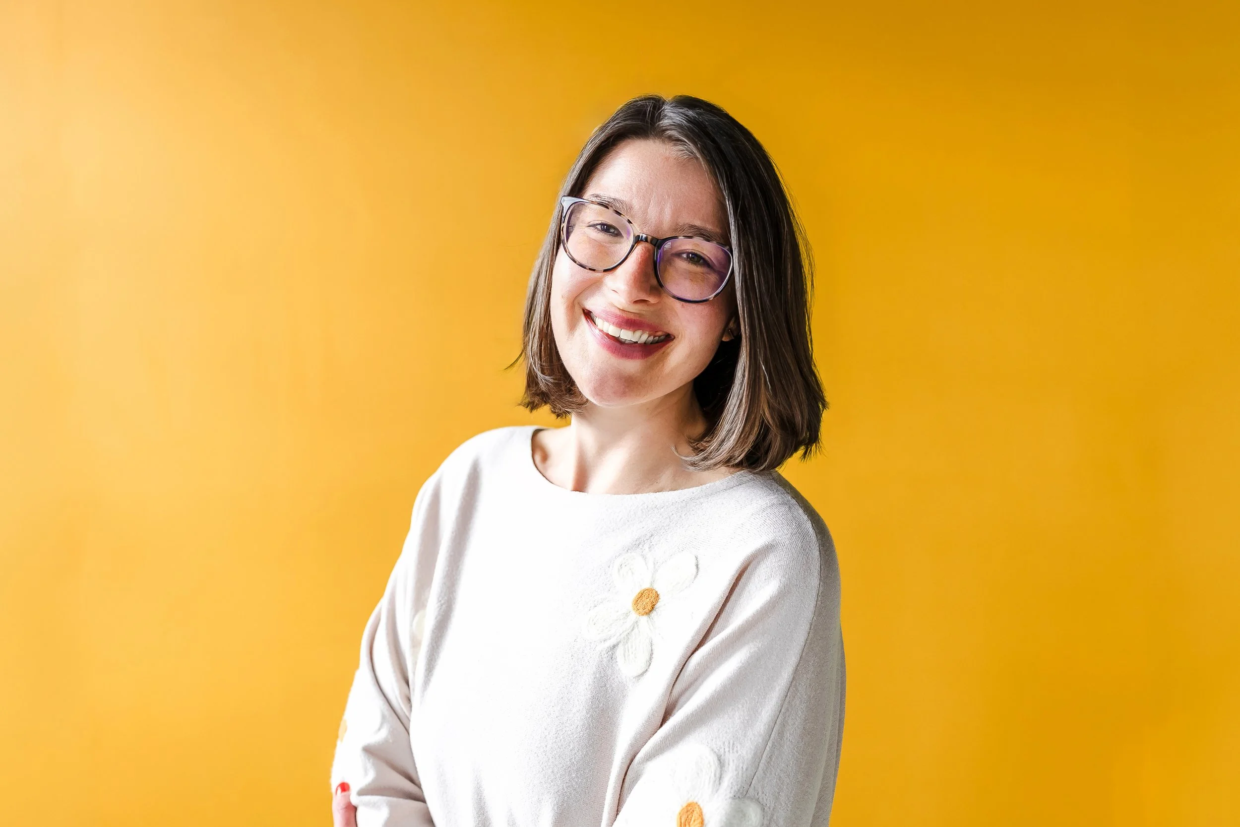 Executive function coach Sarah smiling at the camera in front of a yellow background