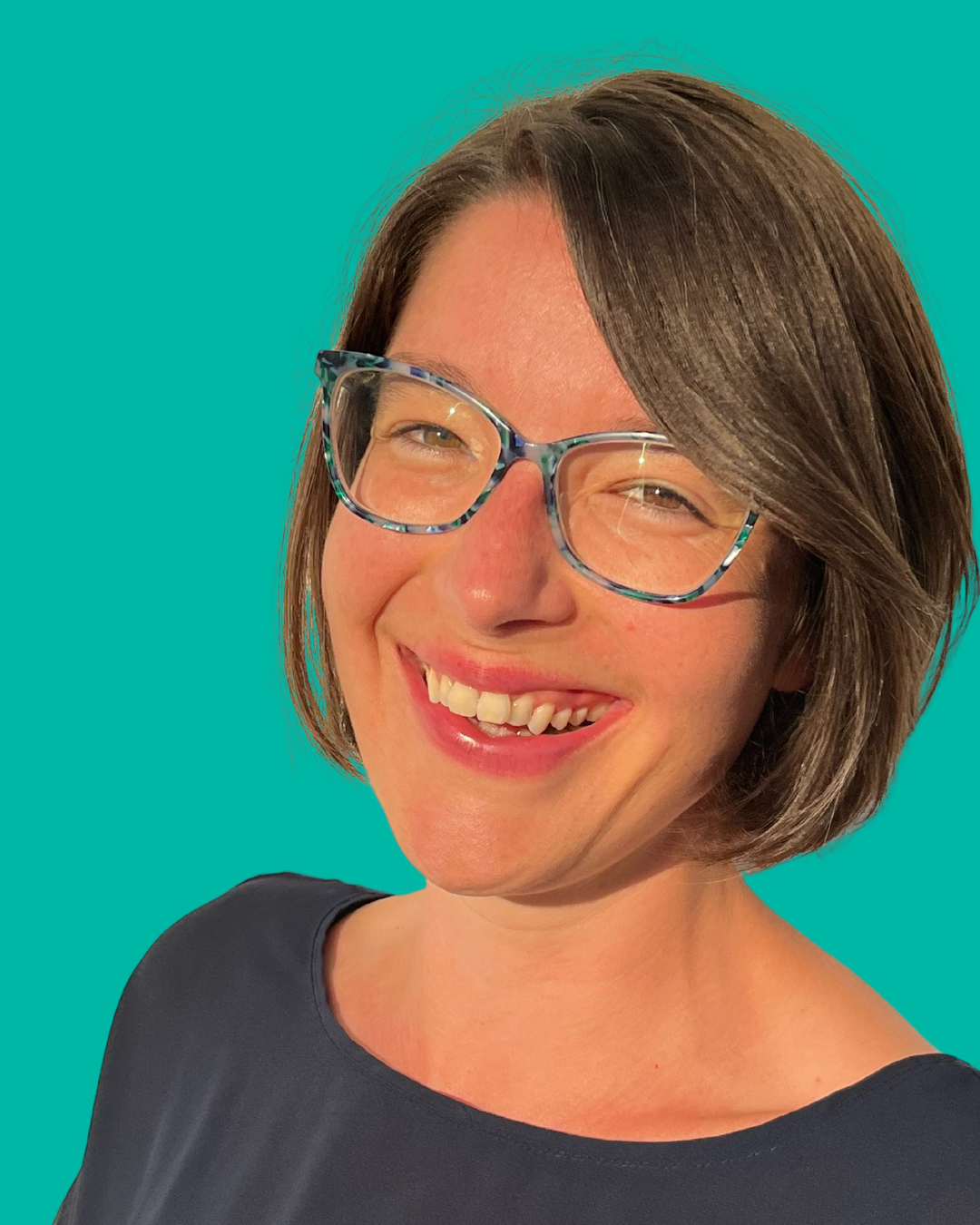 Smiling woman with short brown hair and glasses against teal background.