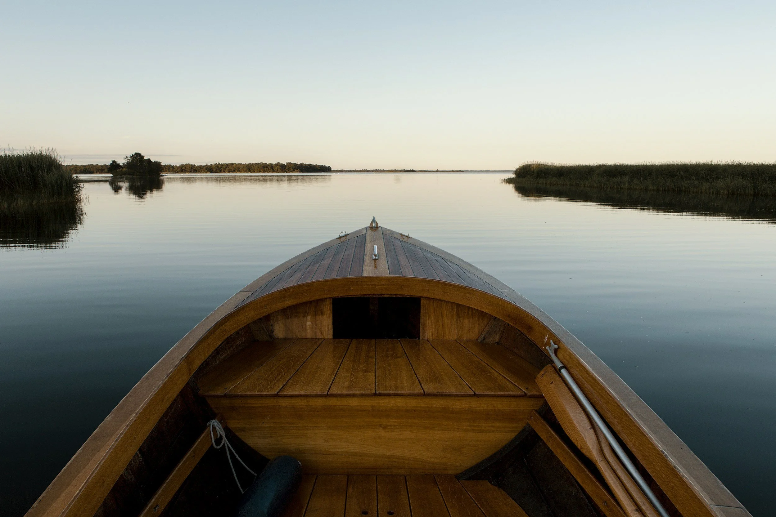 View from a boat on calm water with grassy islands on either side under a clear sky during sunset or sunrise.