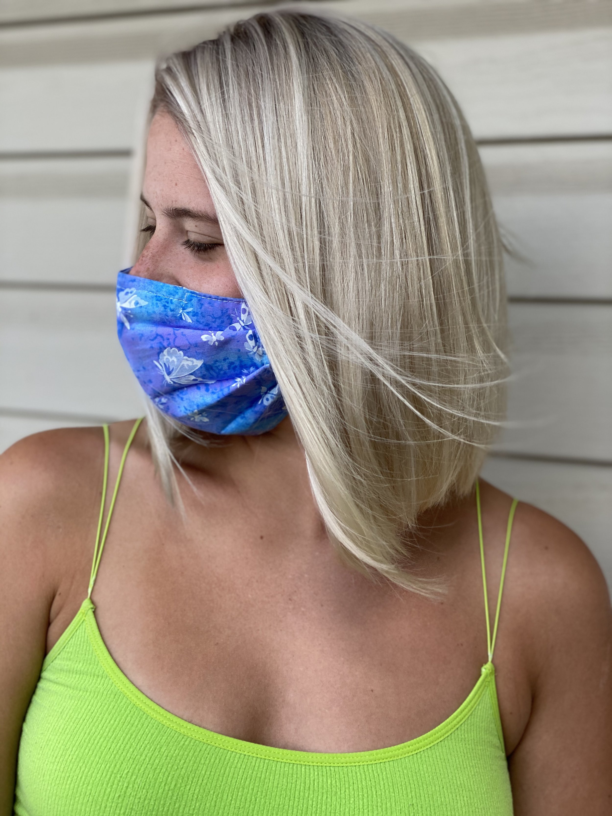 Person wearing a blue face mask and lime green tank top against a light-colored wall