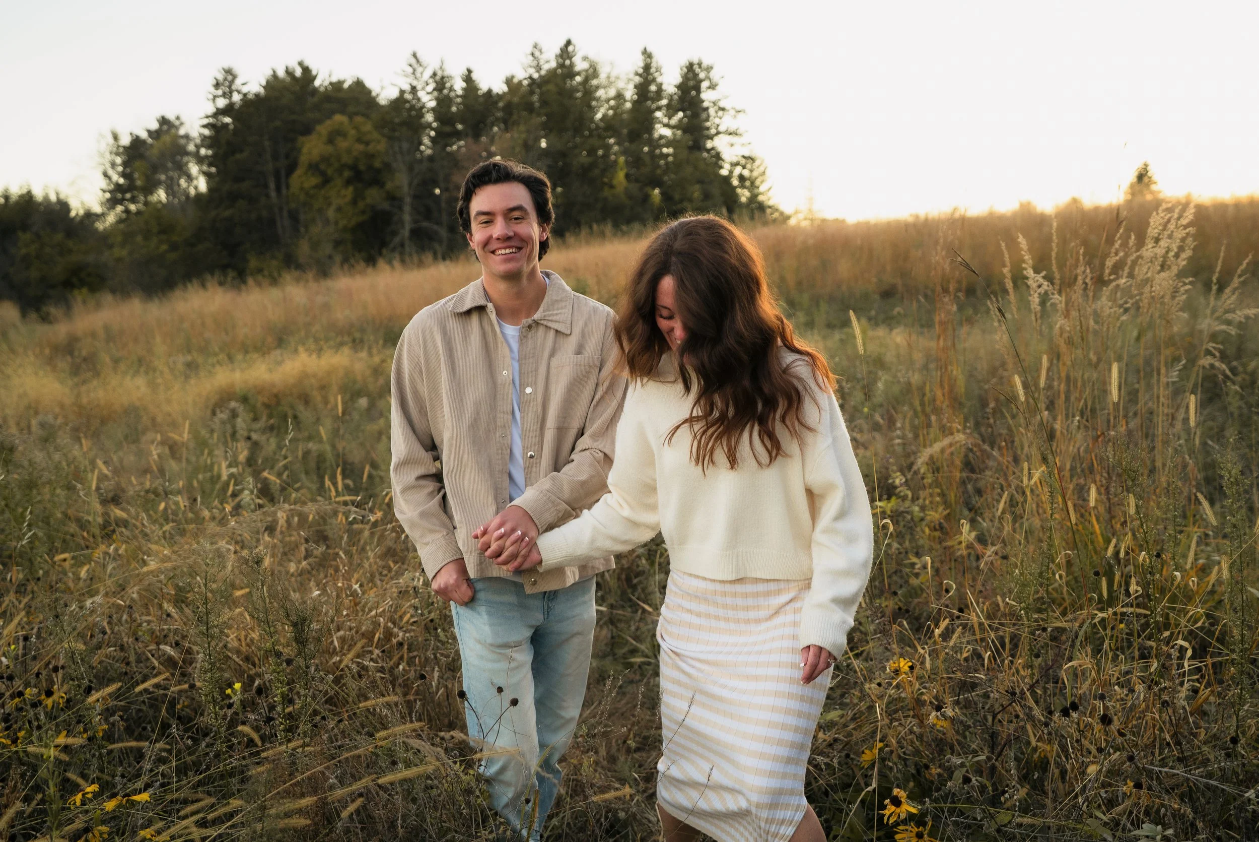 A couple holding hands and walking through a grassy field at sunset