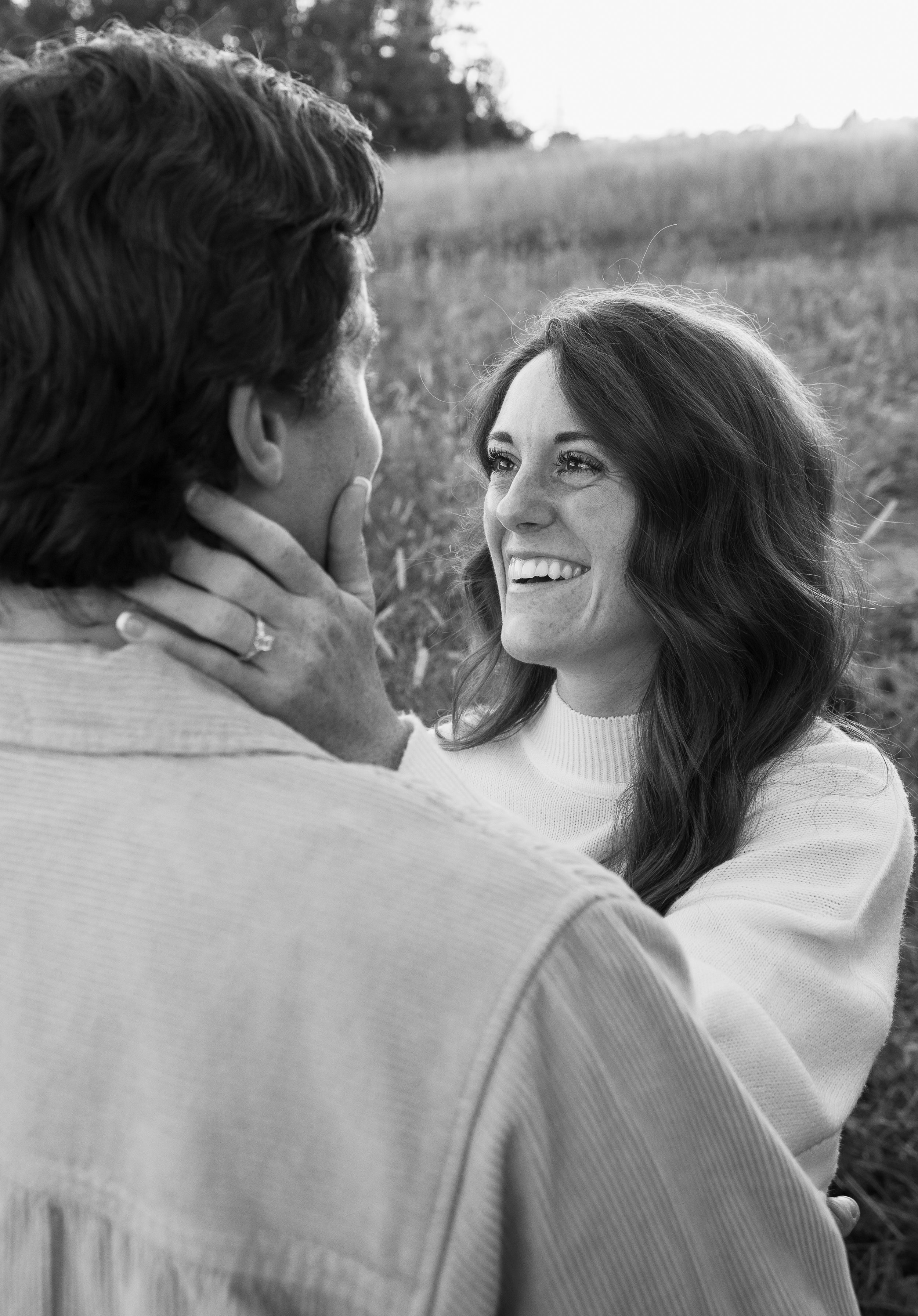 A woman smiling at a man in an outdoor field, holding his face gently.